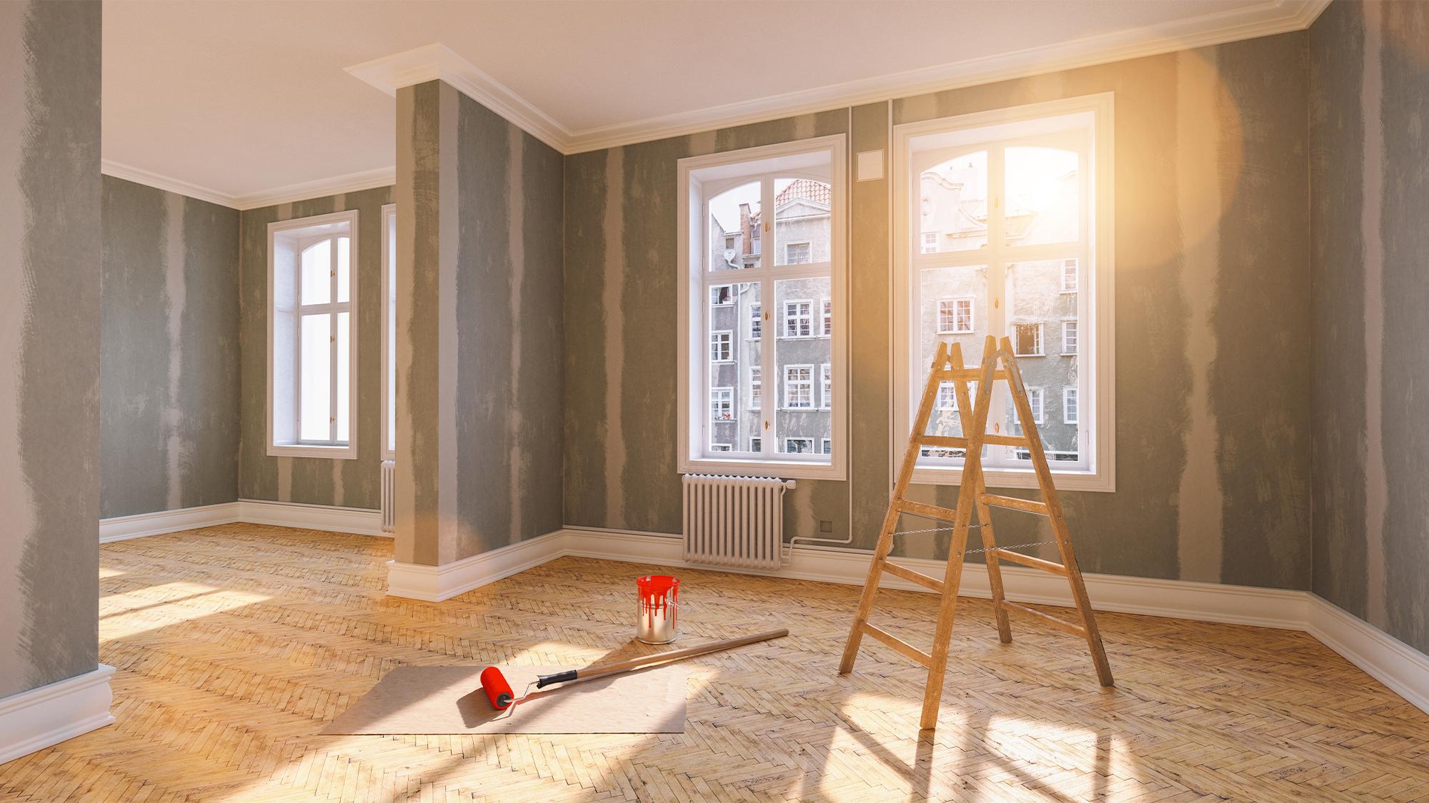 Room under renovation with prepped walls, a ladder, and paint supplies, lit by bright sunlight.