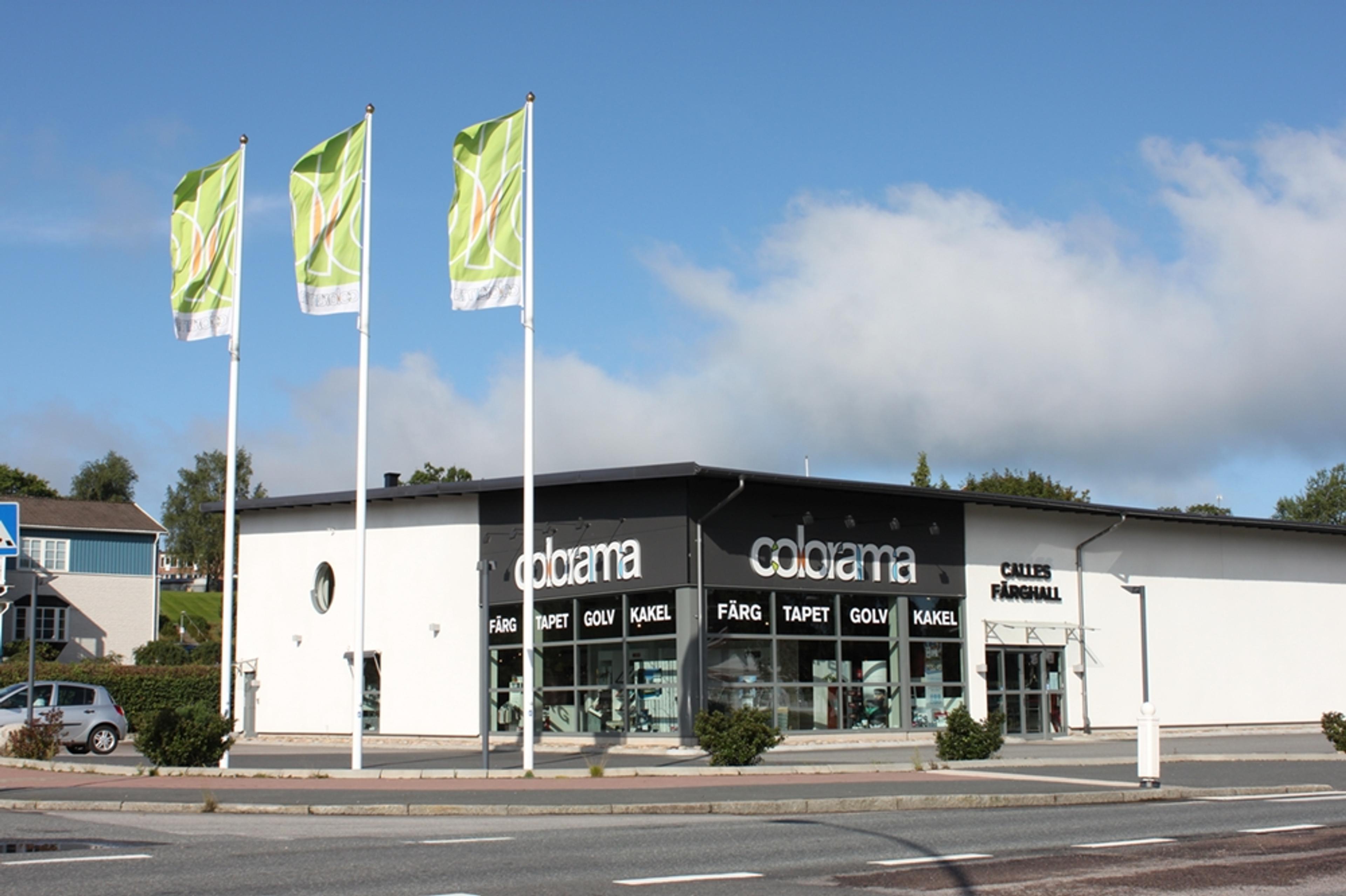 A Colorama paint and home improvement store with three green flags, under a blue sky.