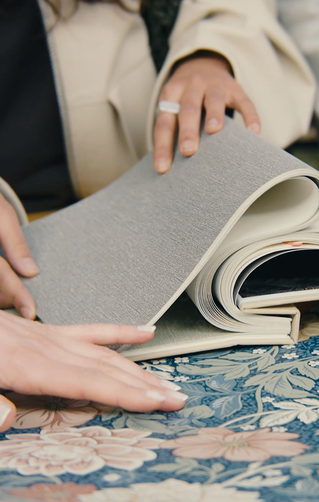 A person's hands holding up a grey textured material sample over a blue and pink floral patterned fabric.