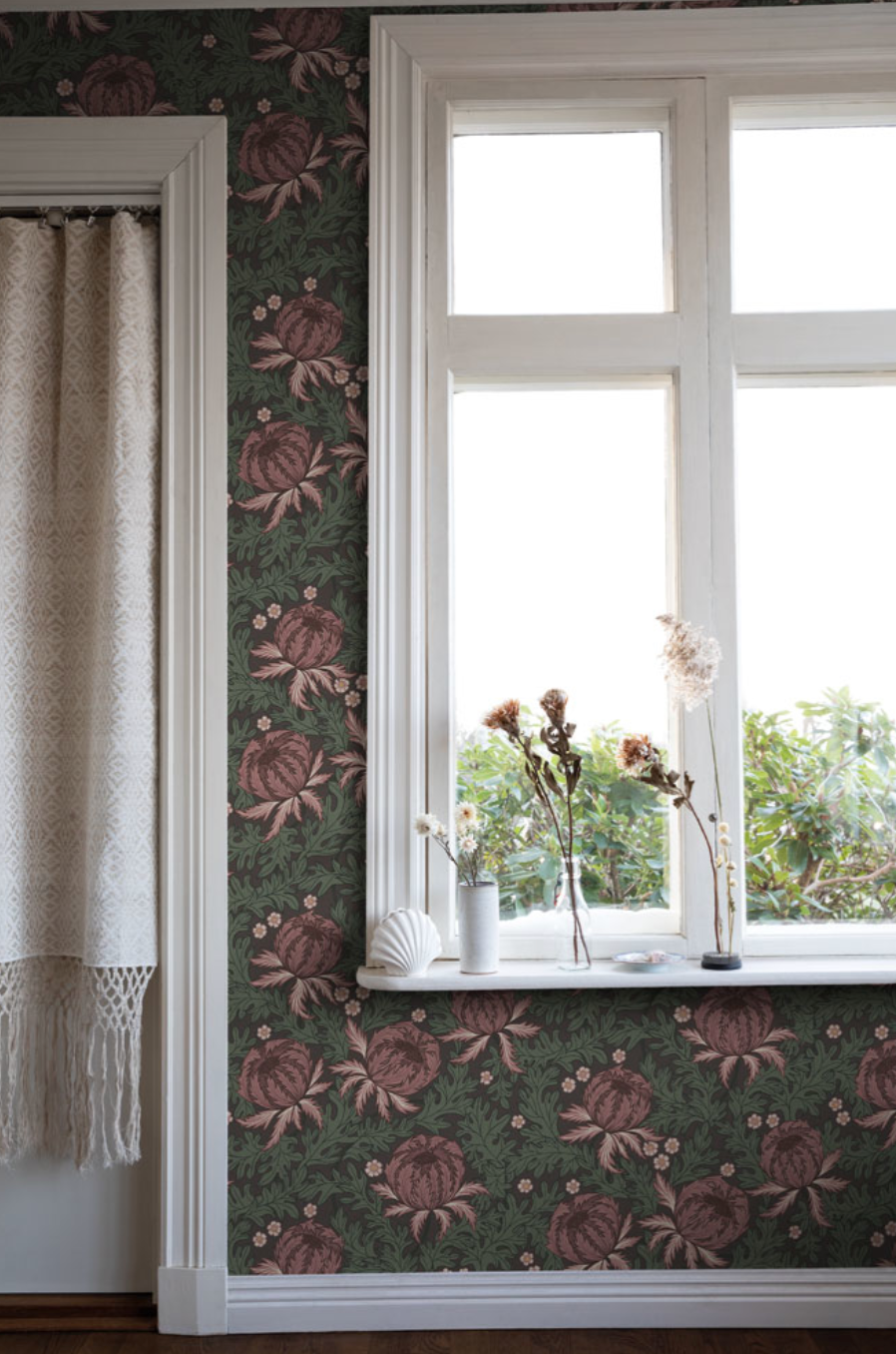 Dark green wallpaper with large maroon floral patterns, a white window with dried flowers on the sill, and a cream curtain with fringe.