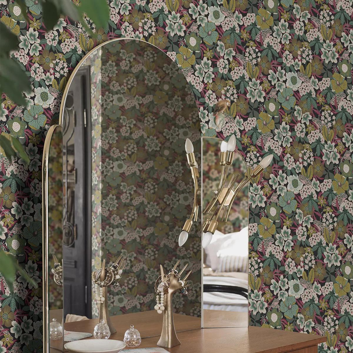 An arched gold-framed mirror on a wooden vanity against dark floral wallpaper, reflecting a room with jewelry displays.