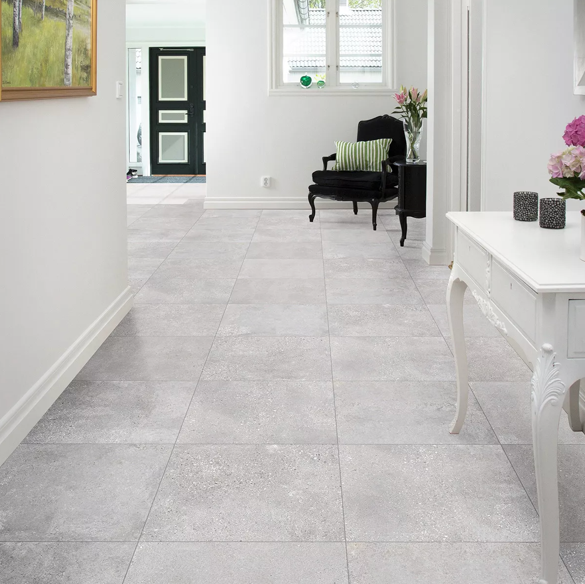 A bright hallway with light gray textured tiles, a white console table, and a black armchair.
