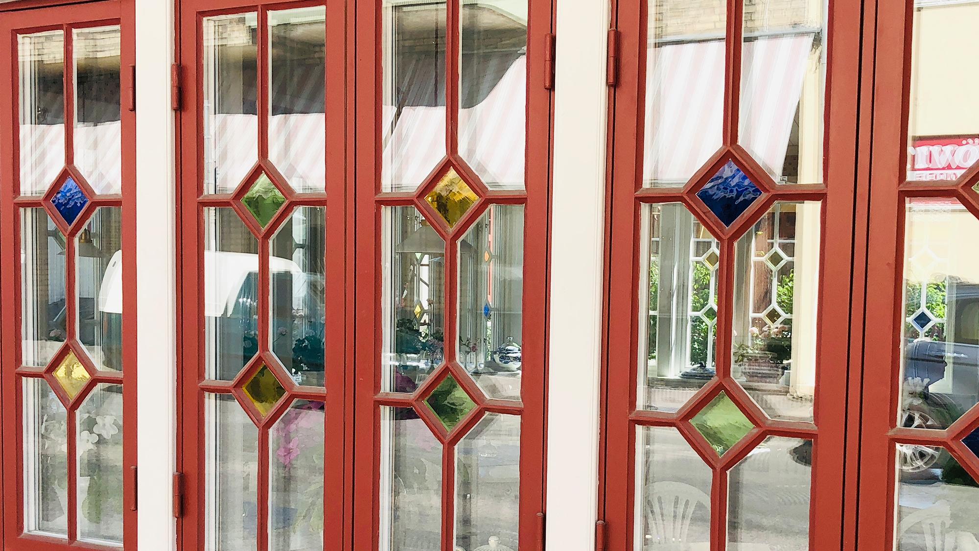 Red-framed glass doors with clear panes and decorative diamond-shaped blue, yellow, and green colored glass accents.