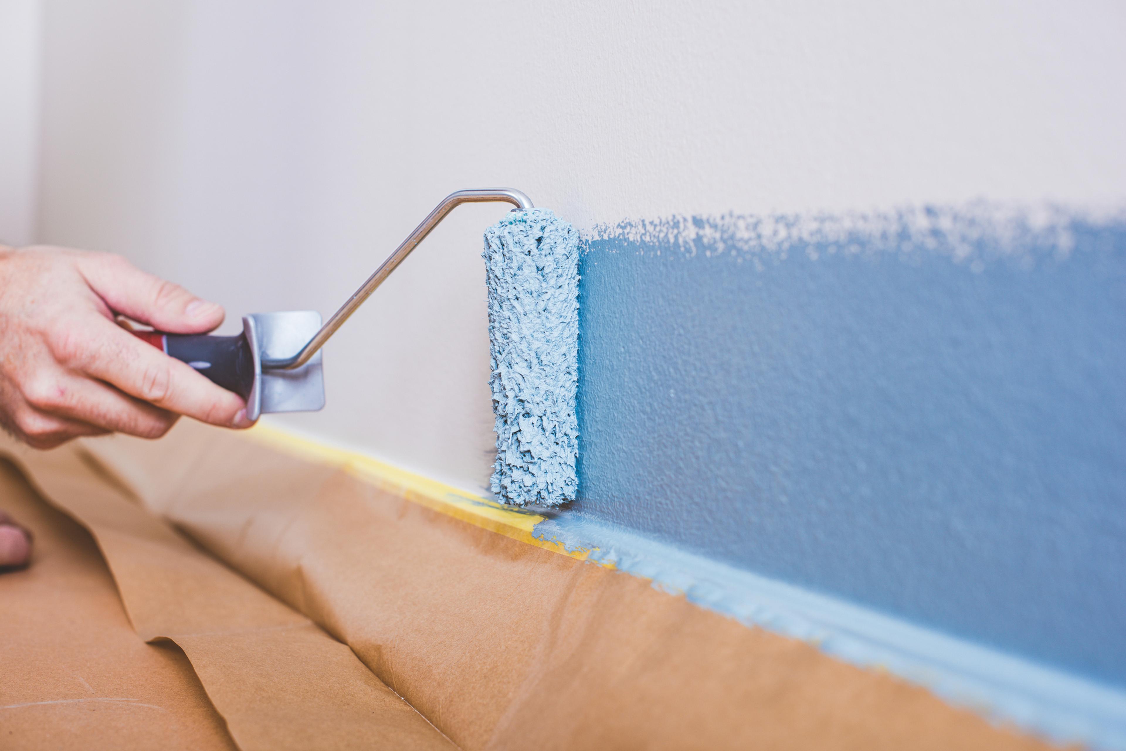 Hand painting a white wall blue with a roller.
