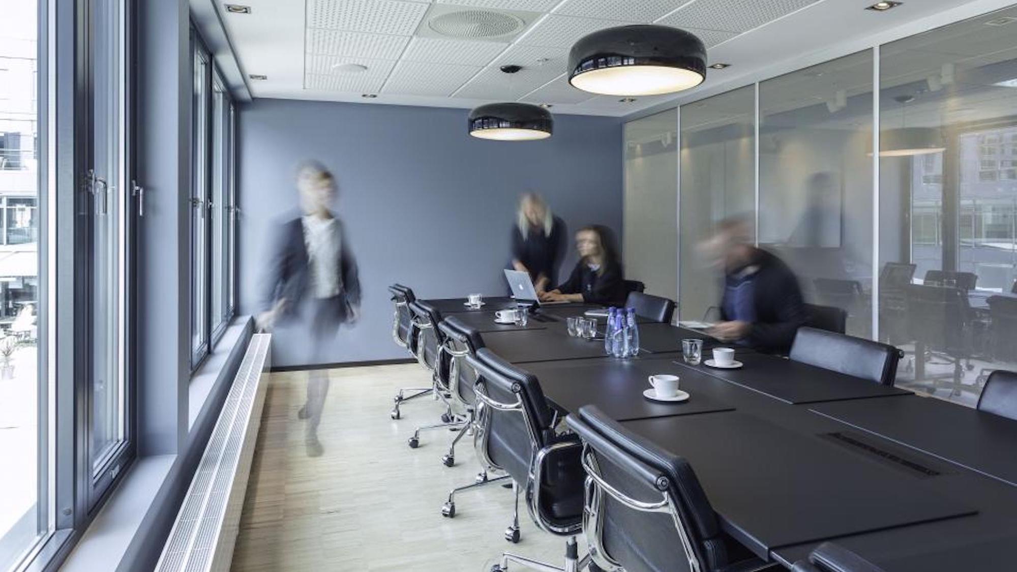 A modern conference room with a long table and motion-blurred people.