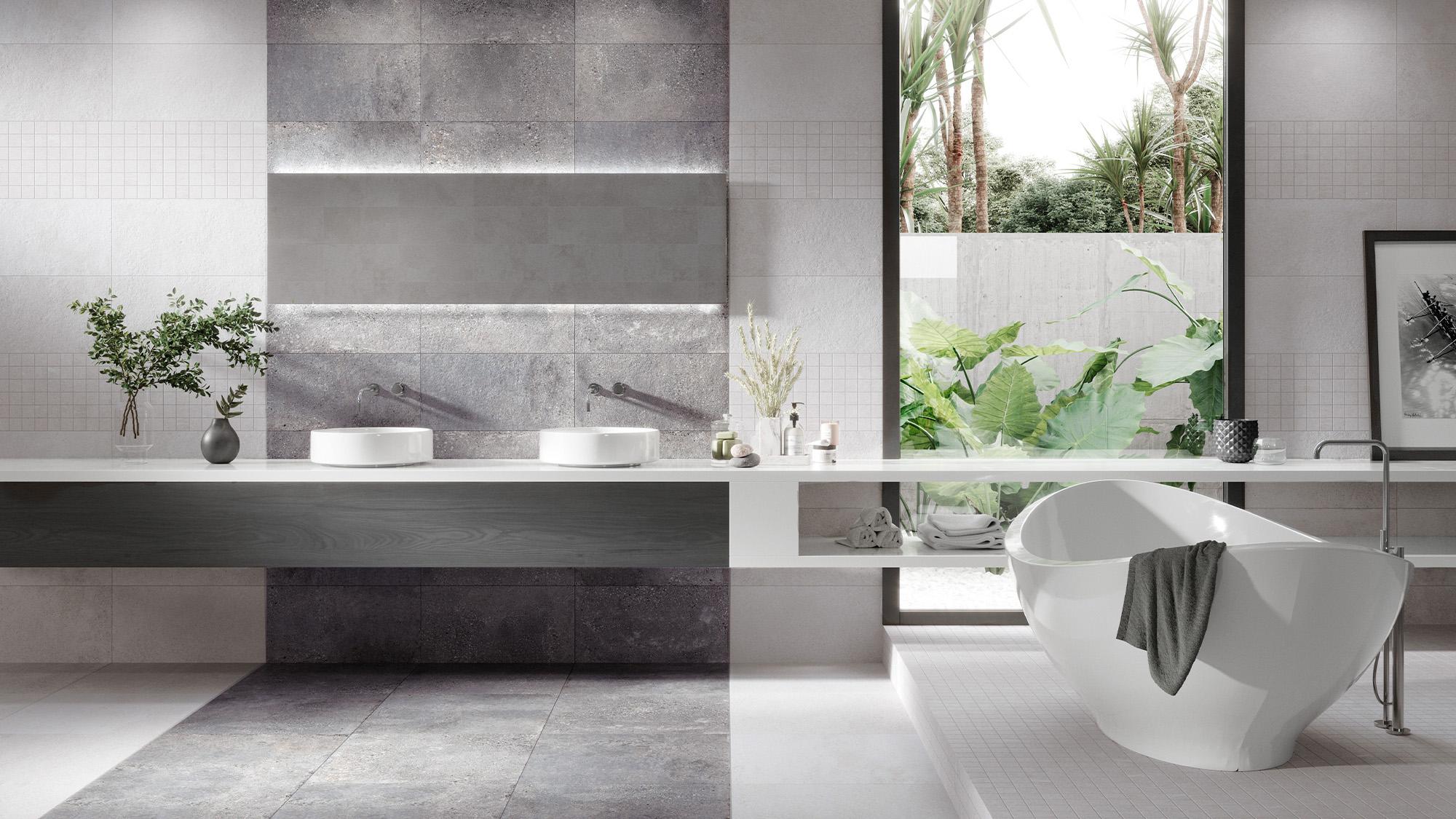 Modern bathroom with double vanity, freestanding tub, grey tiled walls, and garden view window.