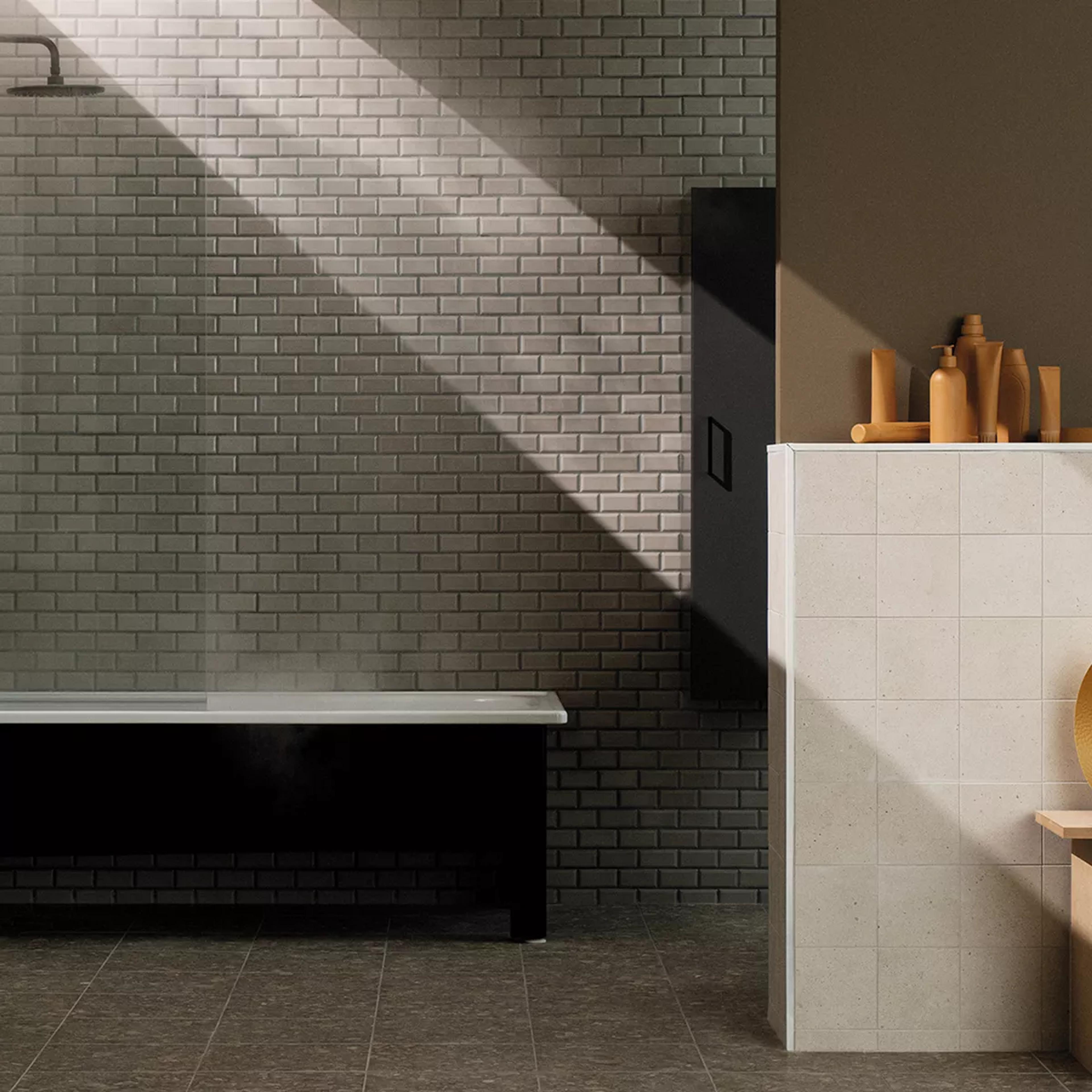 A modern bathroom with a black bathtub emitting steam, grey subway tile walls, and a light-tiled partition displaying tan bathroom products, illuminated by a diagonal beam of sunlight.