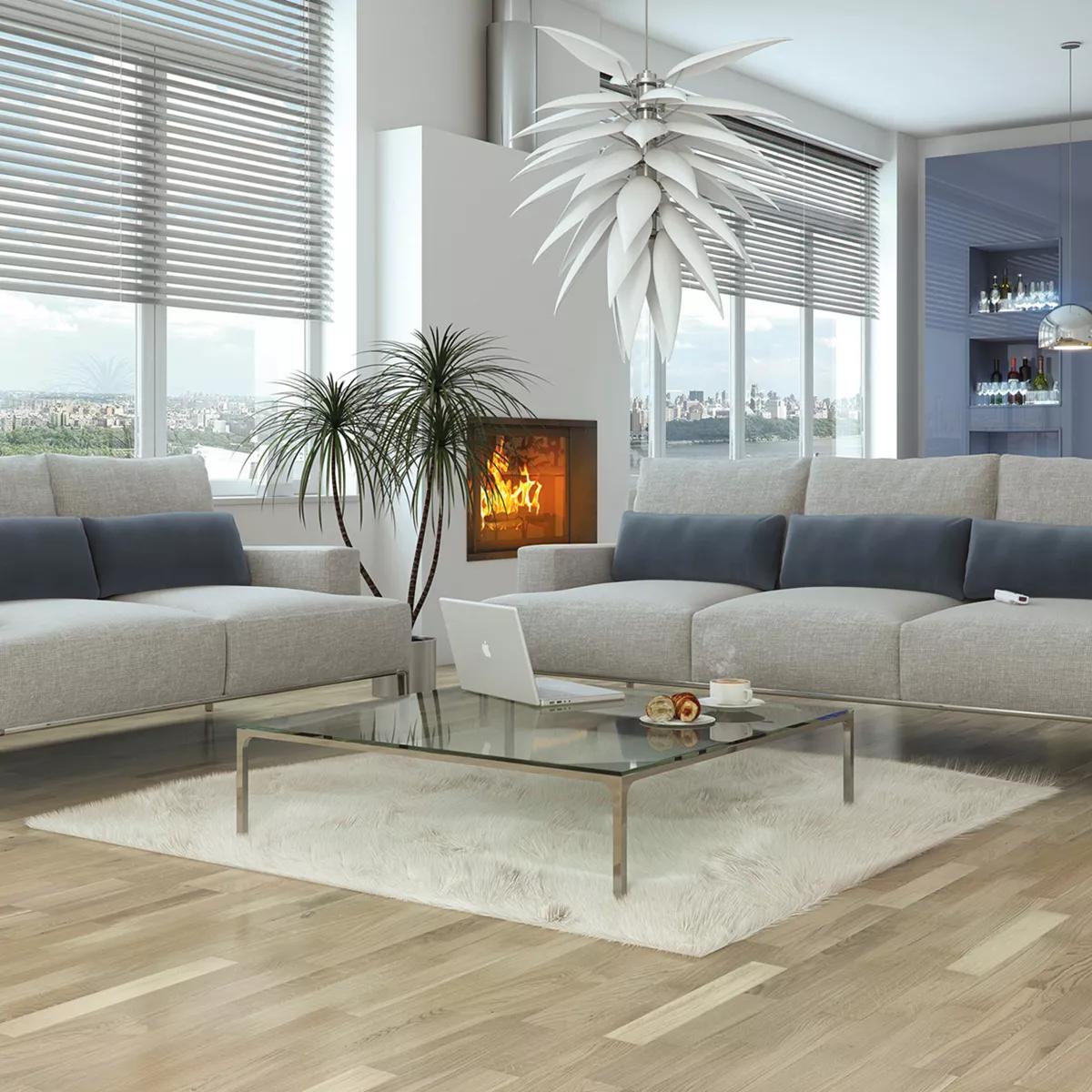 A chic, modern living room with light grey sofas, a glass coffee table, a lit fireplace, a sculptural white ceiling light, and city views from large windows.