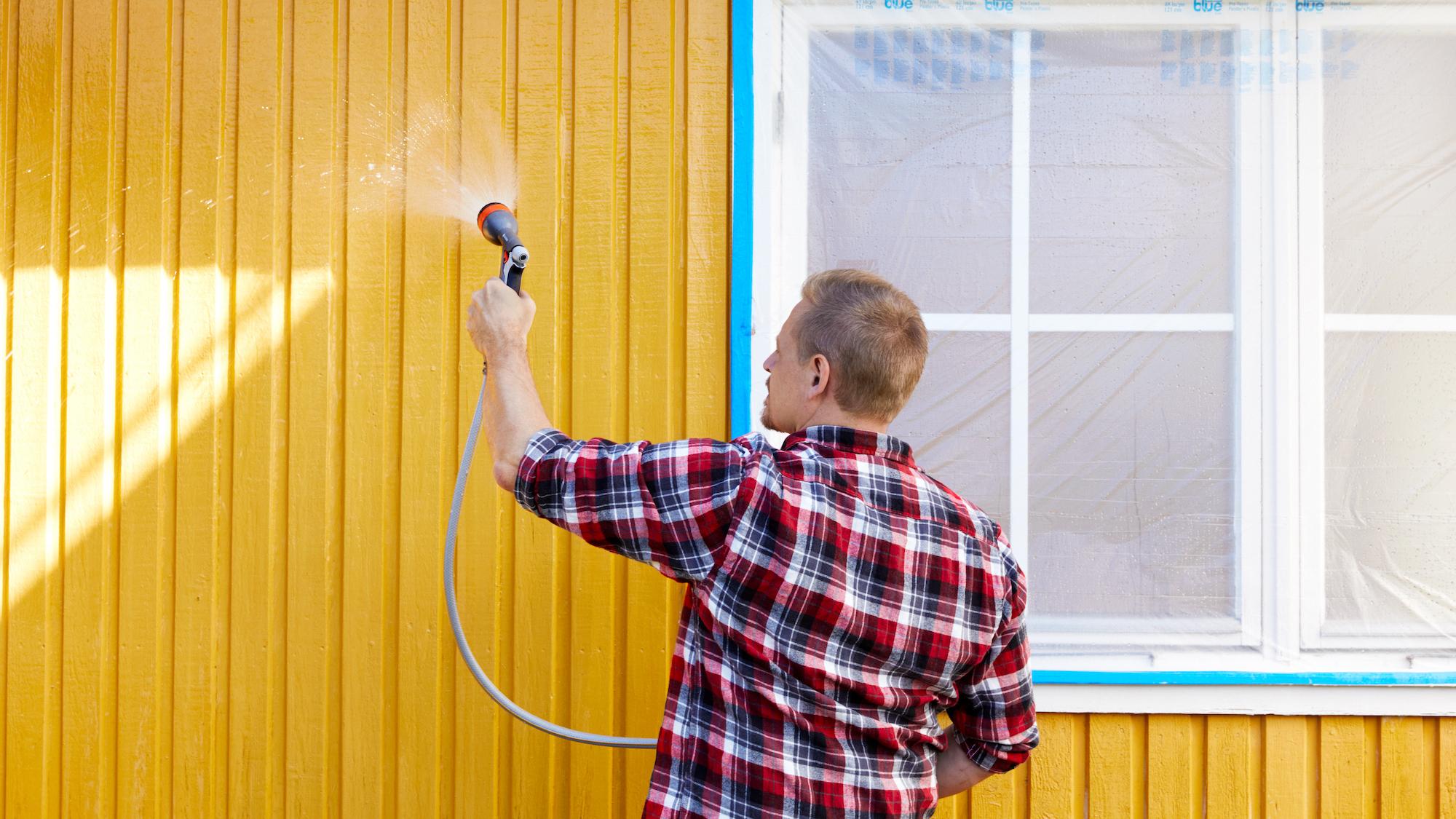 Man power washing a yellow house wall.