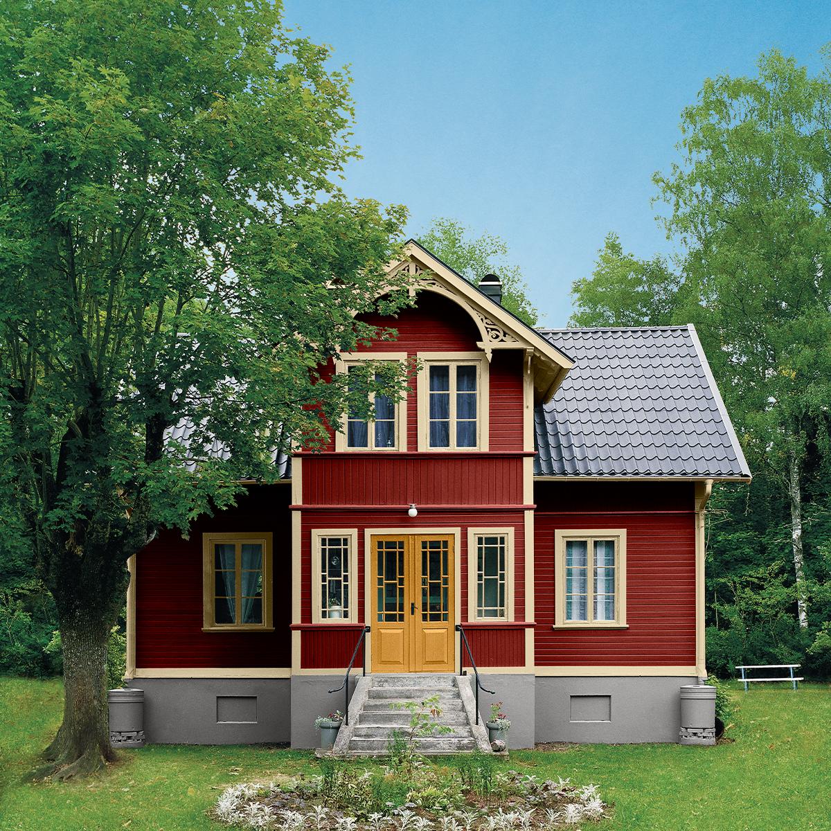 Red house with yellow trim and decorative gables, surrounded by green trees and grass.