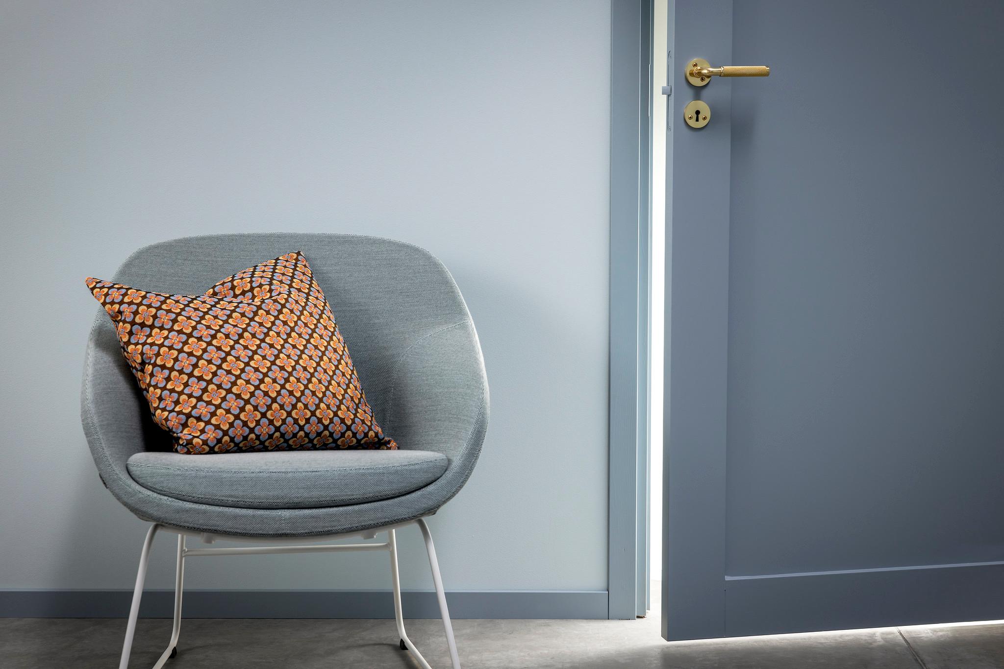 A grey armchair with a patterned pillow sits next to a slightly ajar dark blue door.