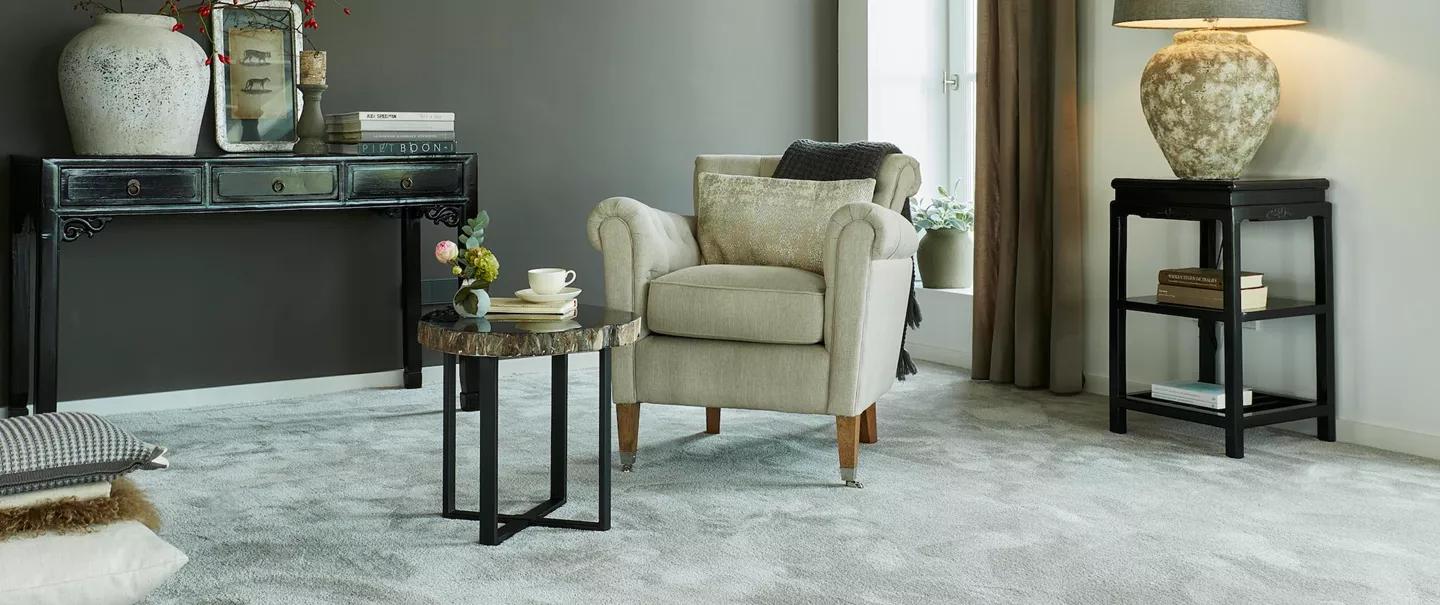 A stylish living room featuring a plush light grey carpet, a beige armchair, and elegant dark wood furniture.
