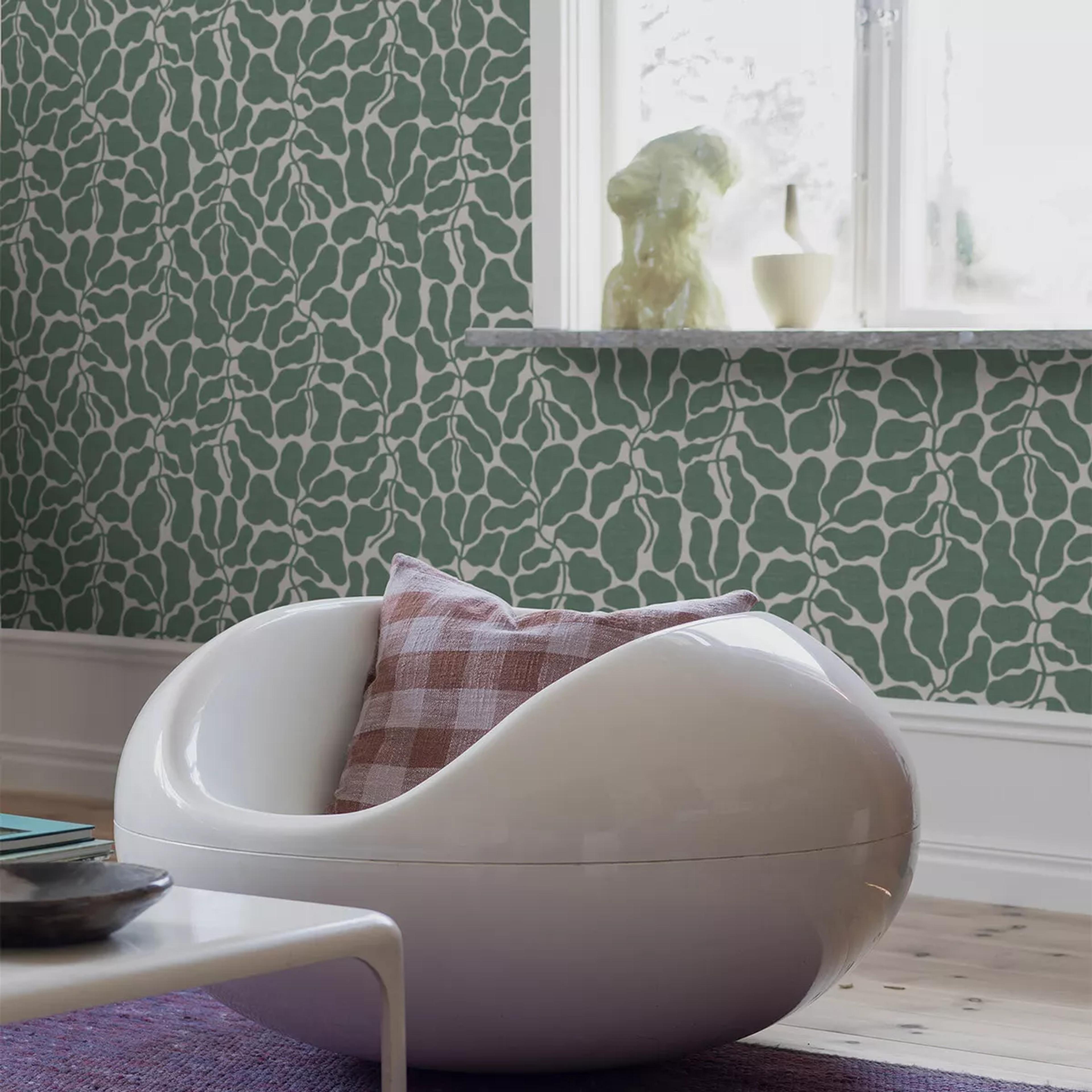 A modern white egg chair with a plaid pillow in a room featuring green leaf-patterned wallpaper.