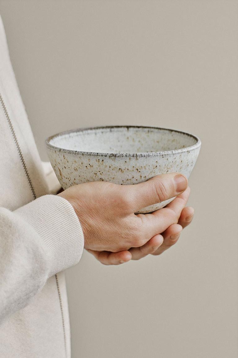 Hands holding a speckled ceramic bowl.