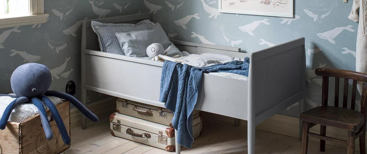 A child's room with a grey daybed, blue whale-patterned wallpaper, and a large blue octopus plush toy.