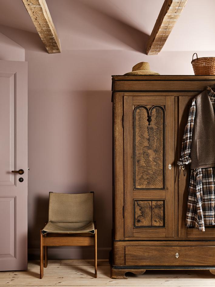 A living room with dark green walls, a pink sofa, a marble coffee table, and a large arched window with sunlight.