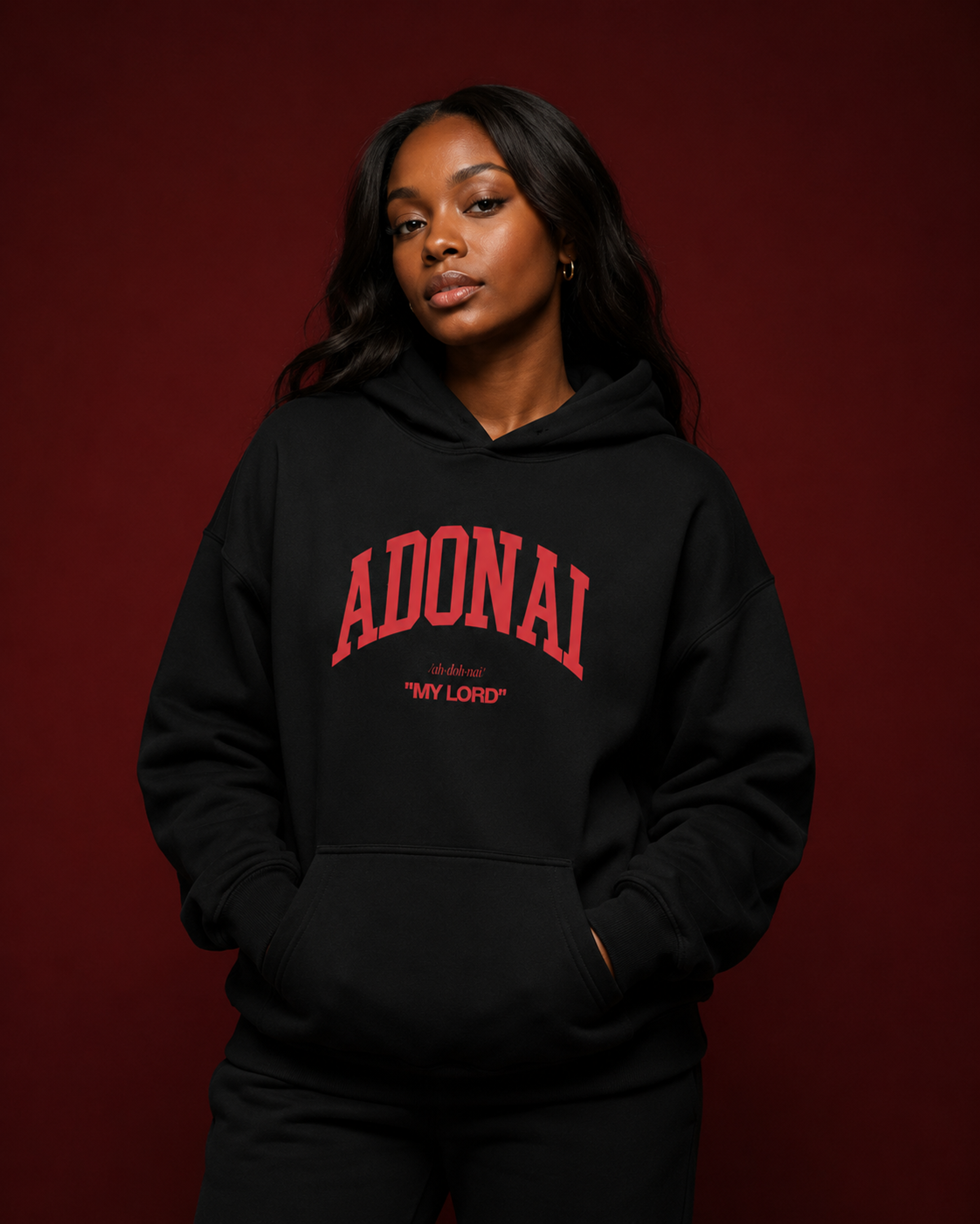 Black oversized hoodie featuring bold red “ADONAI” lettering with the phrase “My Lord” underneath, displayed against a deep burgundy studio background with soft luxury lighting.