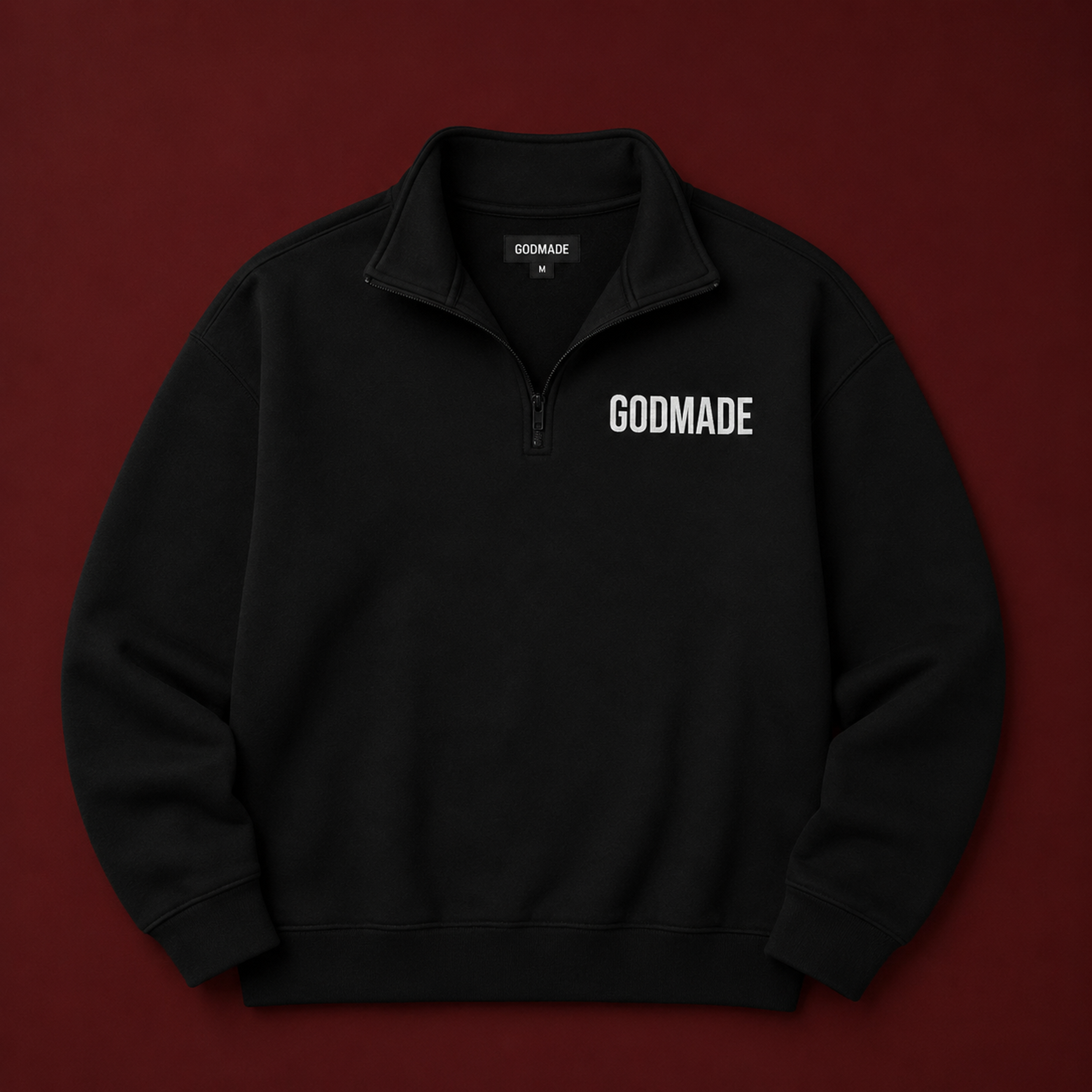 Black GODMADE quarter-zip pullover displayed on a deep burgundy background, featuring a minimalist white chest logo, structured collar, and premium oversized fit.