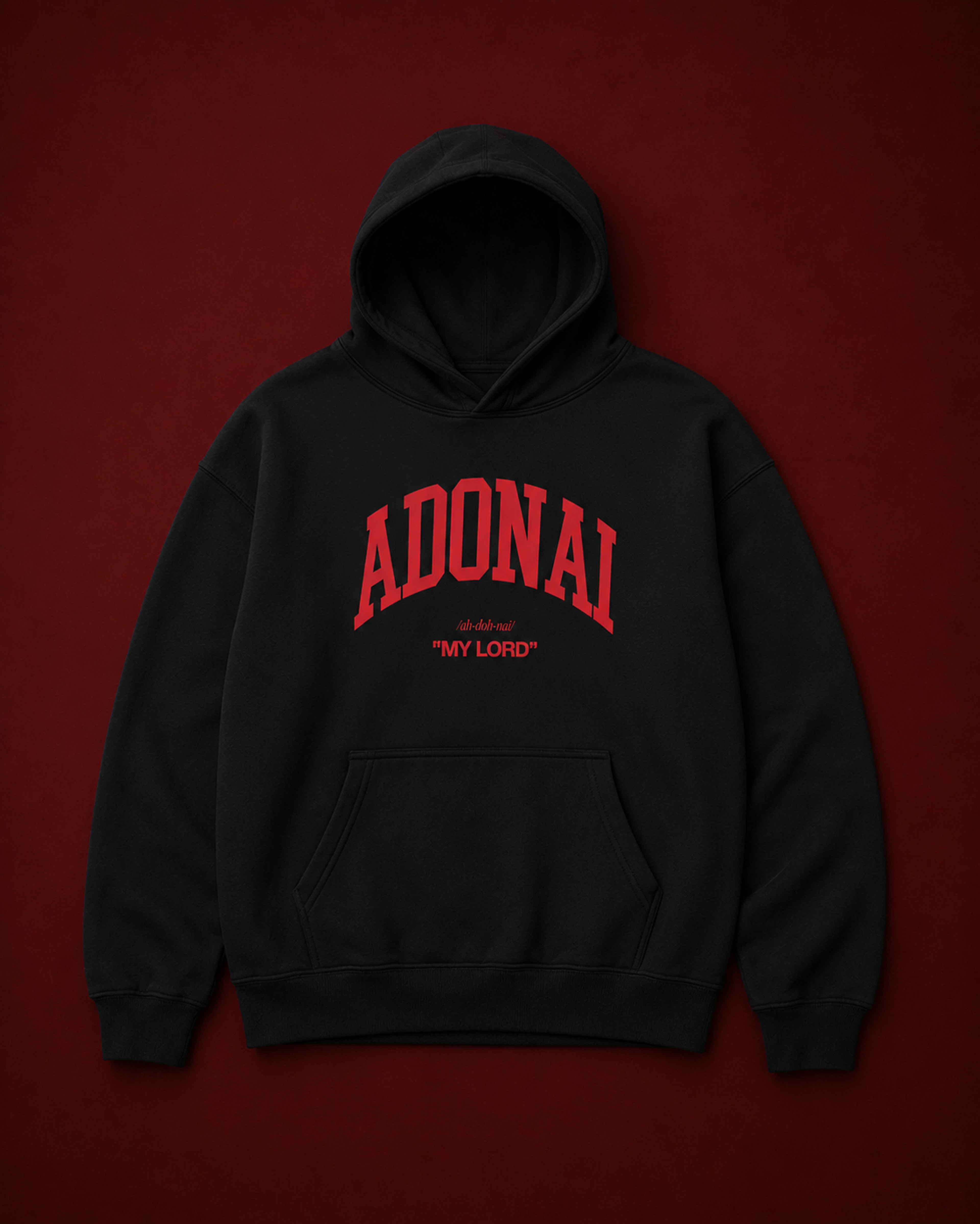 Black oversized hoodie featuring bold red “ADONAI” lettering with the phrase “My Lord” underneath, displayed against a deep burgundy studio background with soft luxury lighting.