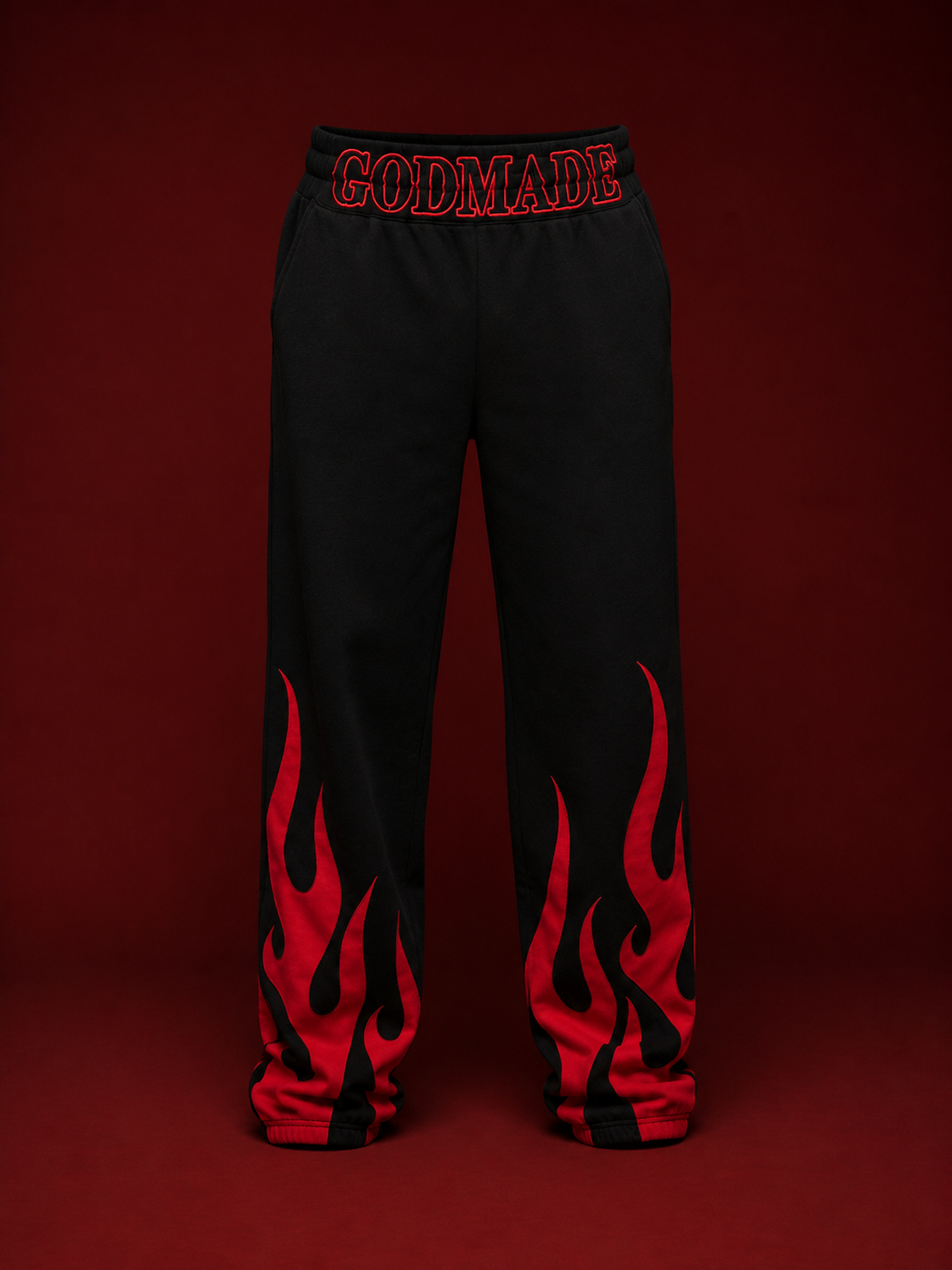 Black GODMADE sweatpants featuring bold red flame graphics rising from the lower legs and oversized red GODMADE lettering across the waistband