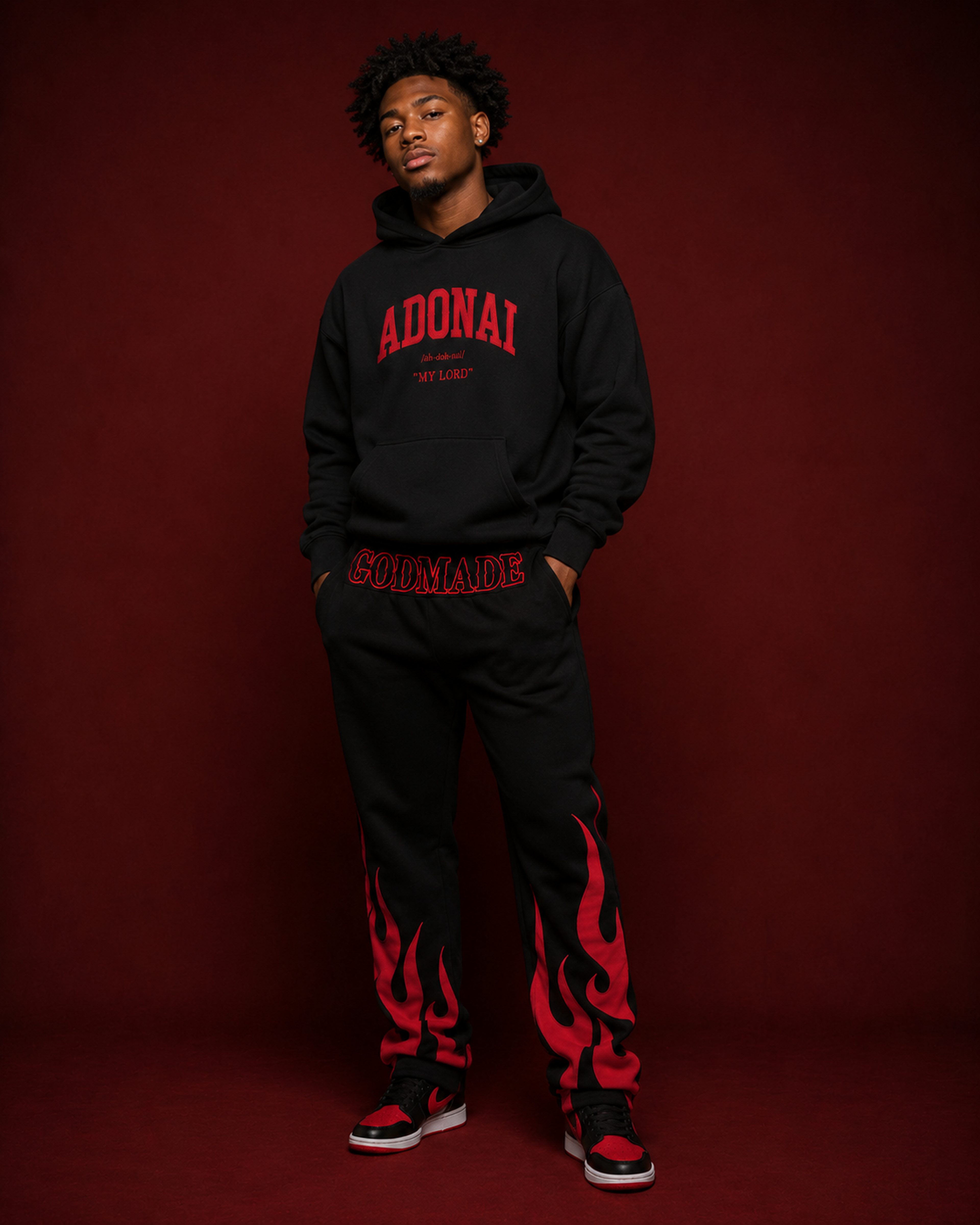 Black GODMADE sweatpants featuring bold red flame graphics rising from the lower legs and oversized red GODMADE lettering across the waistband