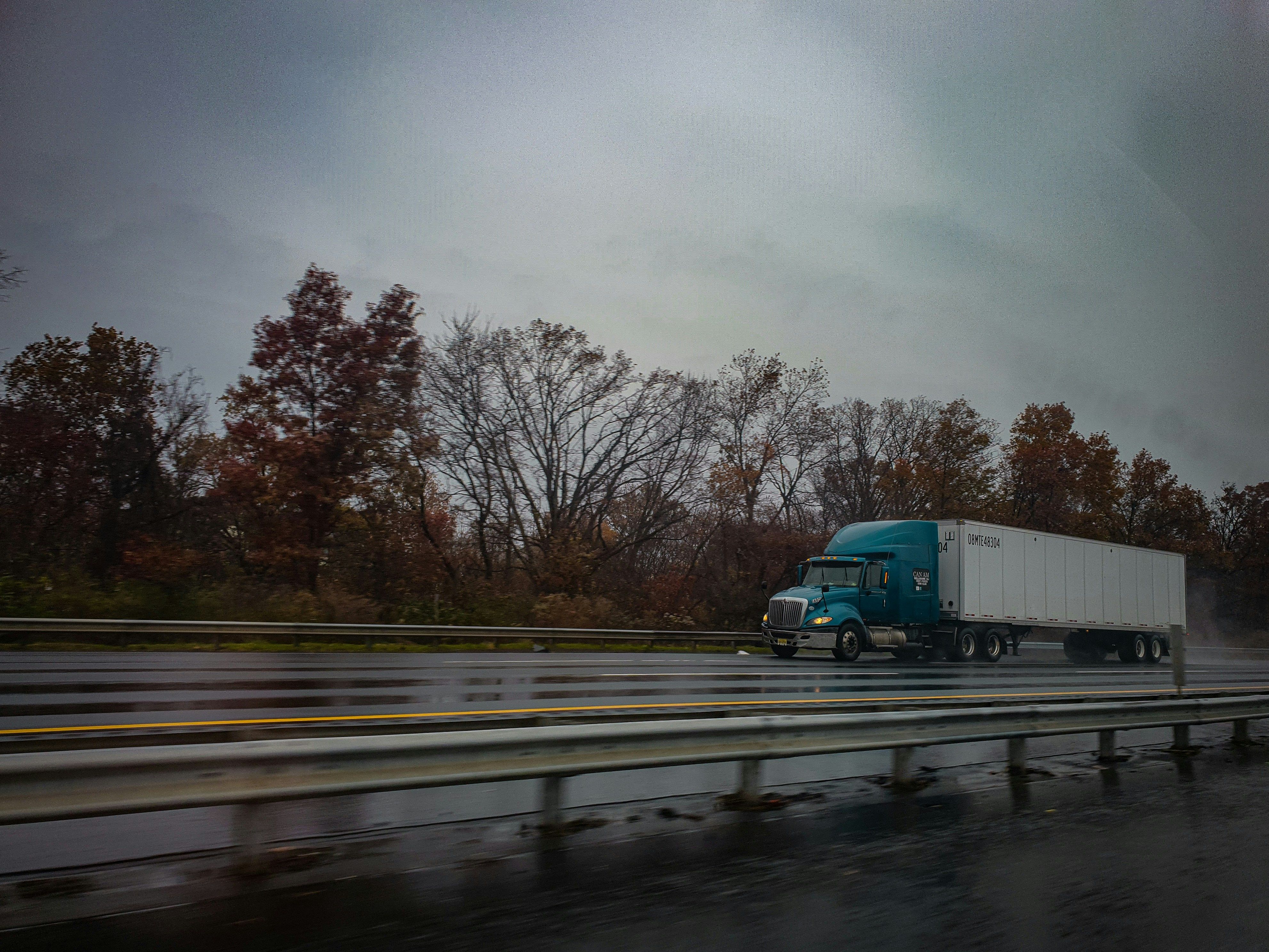 Teal semi truck hauling a white trailer on a wet highway in the rain, showing why you should investigate a trucking company right away after a crash