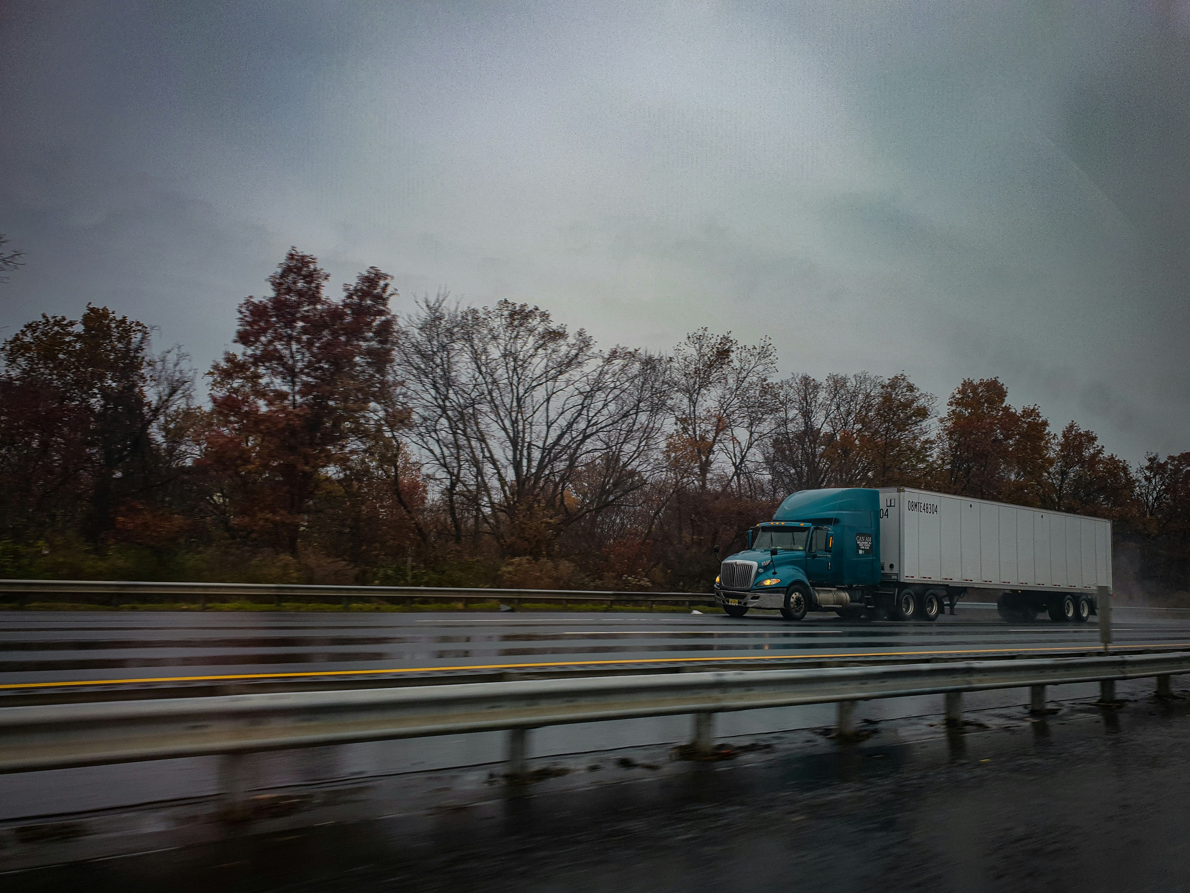 Image Teal semi truck hauling a white trailer on a wet highway in the rain, showing why you should investigate a trucking company right away after a crash