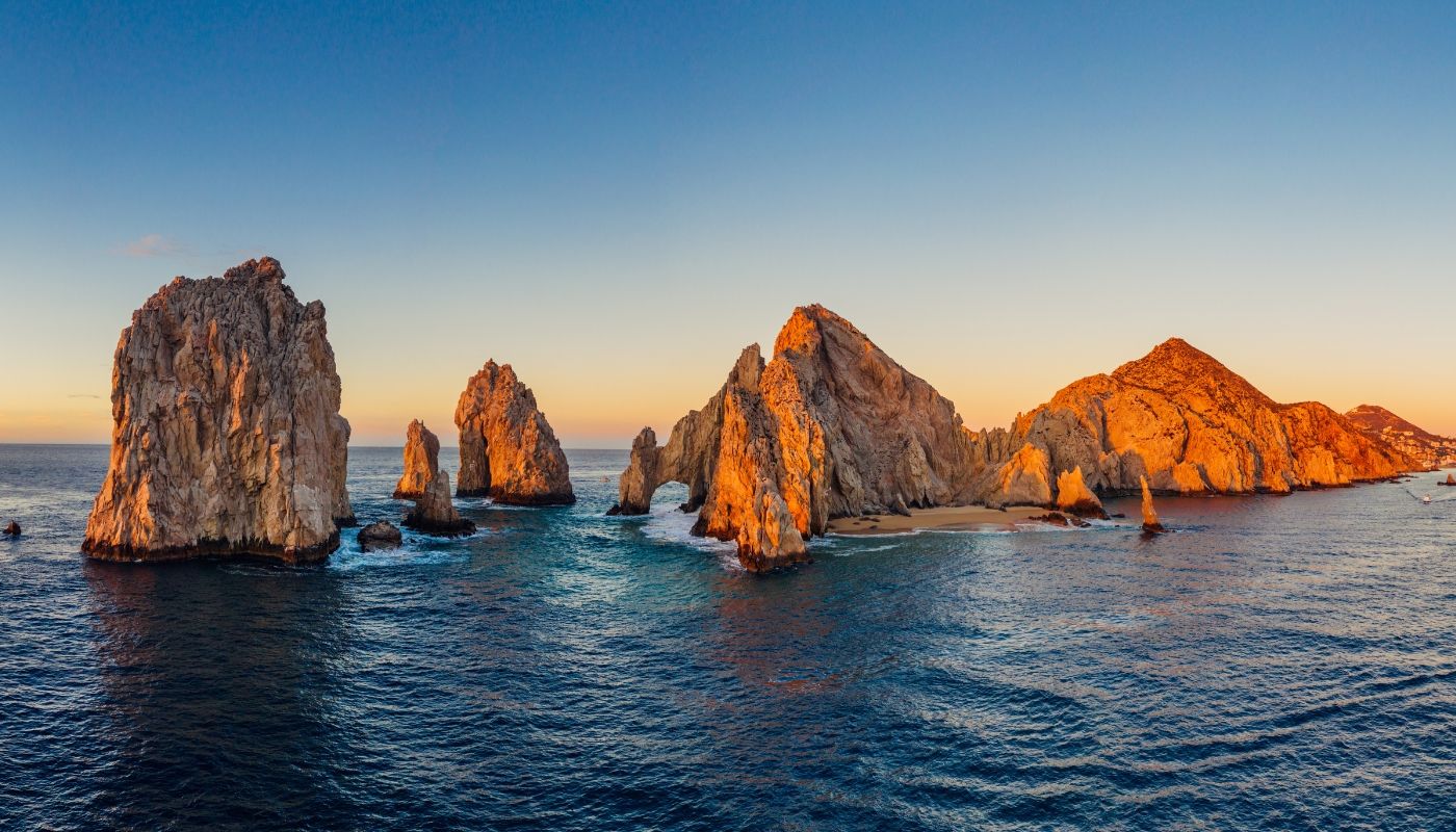 Formaciones rocosas en el mar de Los Cabos al atardecer, con tonos cálidos y vista al océano, representando destinos turísticos en México disponibles en Aeroméxico Vacations
