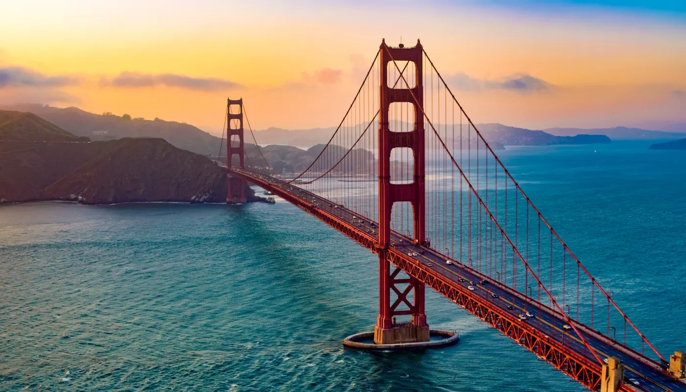 Puente Golden Gate en San Francisco durante el atardecer, rodeado de mar y montañas, representando viajes a Estados Unidos con Aeroméxico Vacations.