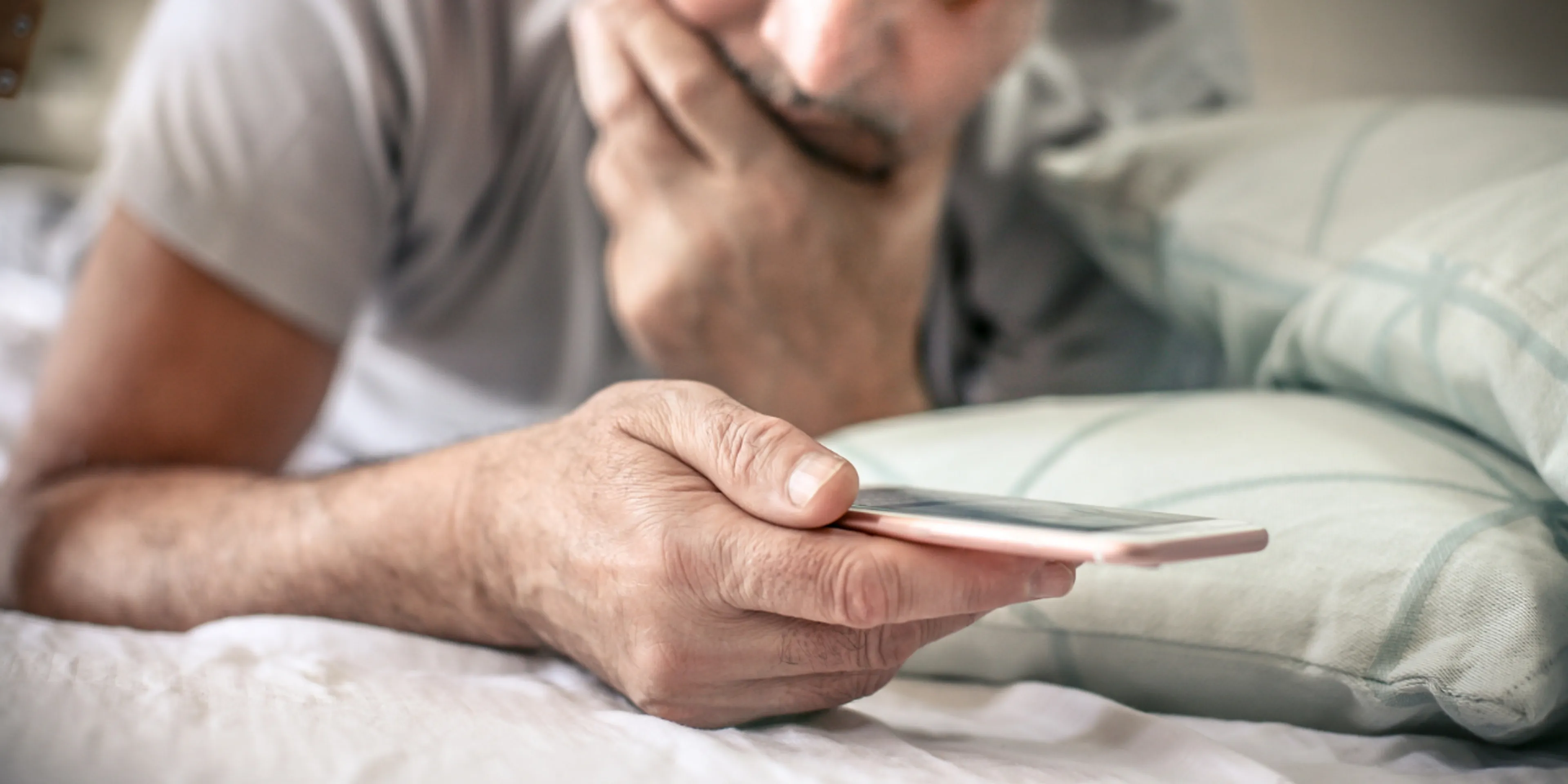Persona con celular en la cama con expresión de preocupación