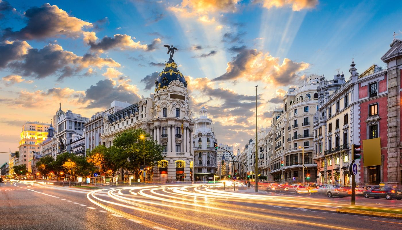 Vista urbana de Madrid con edificios históricos y luces en movimiento al atardecer, representando viajes a destinos internacionales en Europa con Aeroméxico Vacations