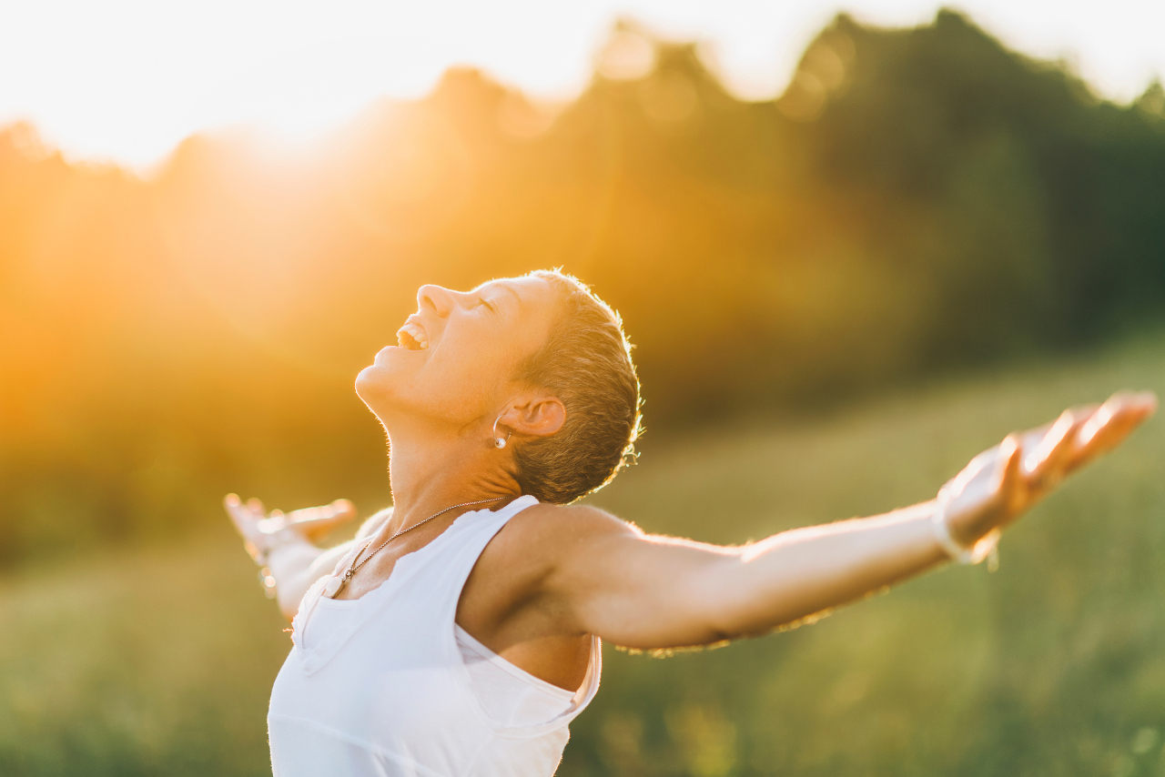 woman looking up at the sky with open arms and a smile