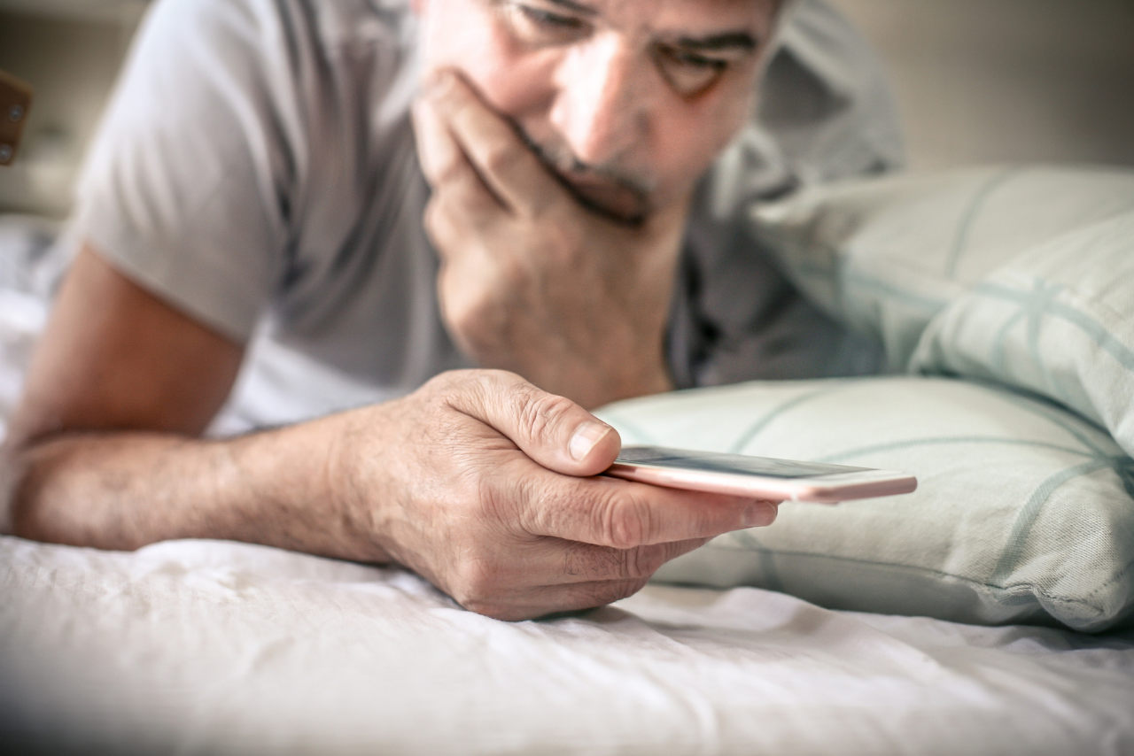 Persona con celular en la cama con expresión de preocupación