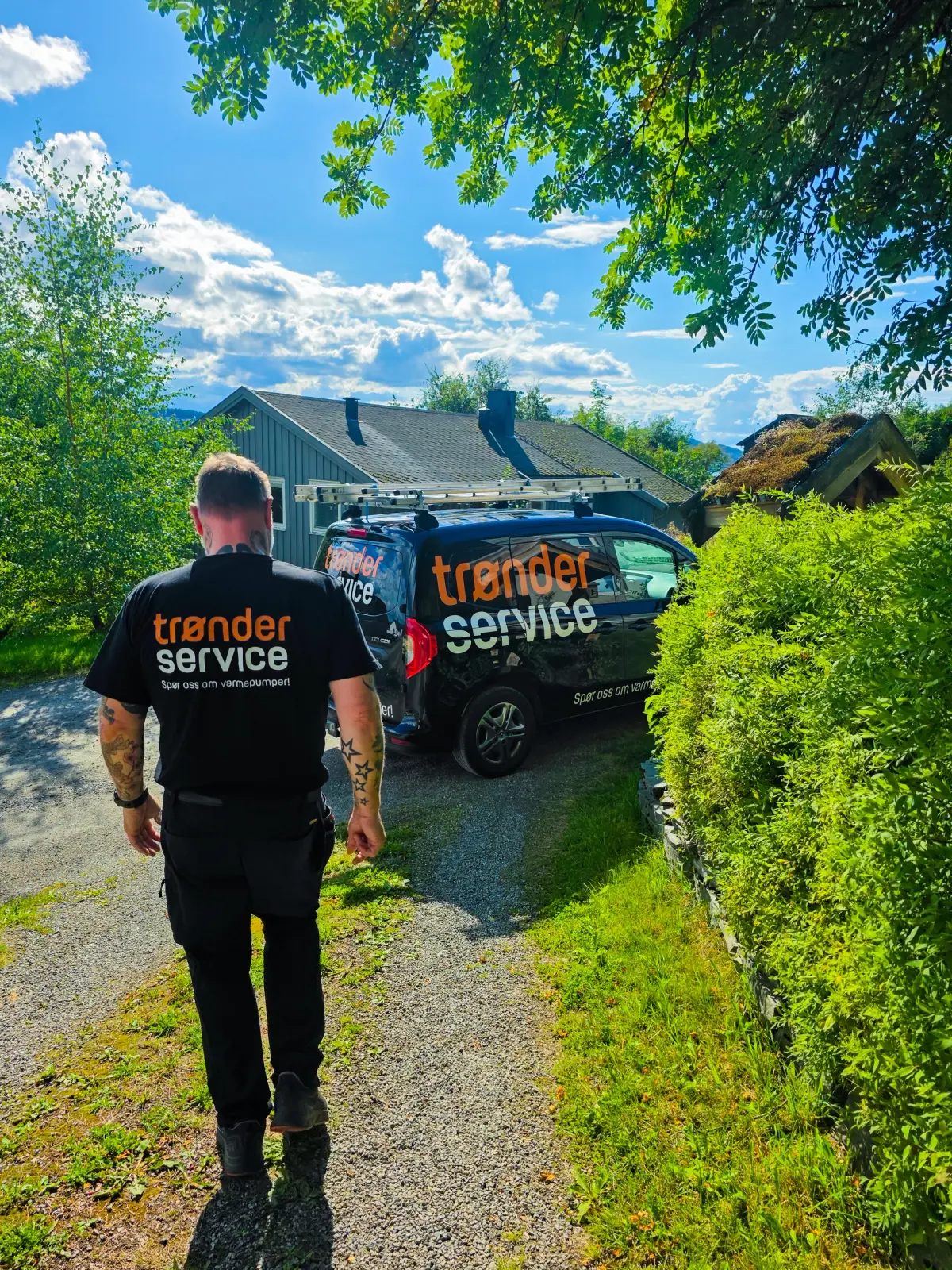To blide servicemontører fra Trønderservice i mørkeblå arbeidsjakker ved en varmepumpe utenfor en bolig