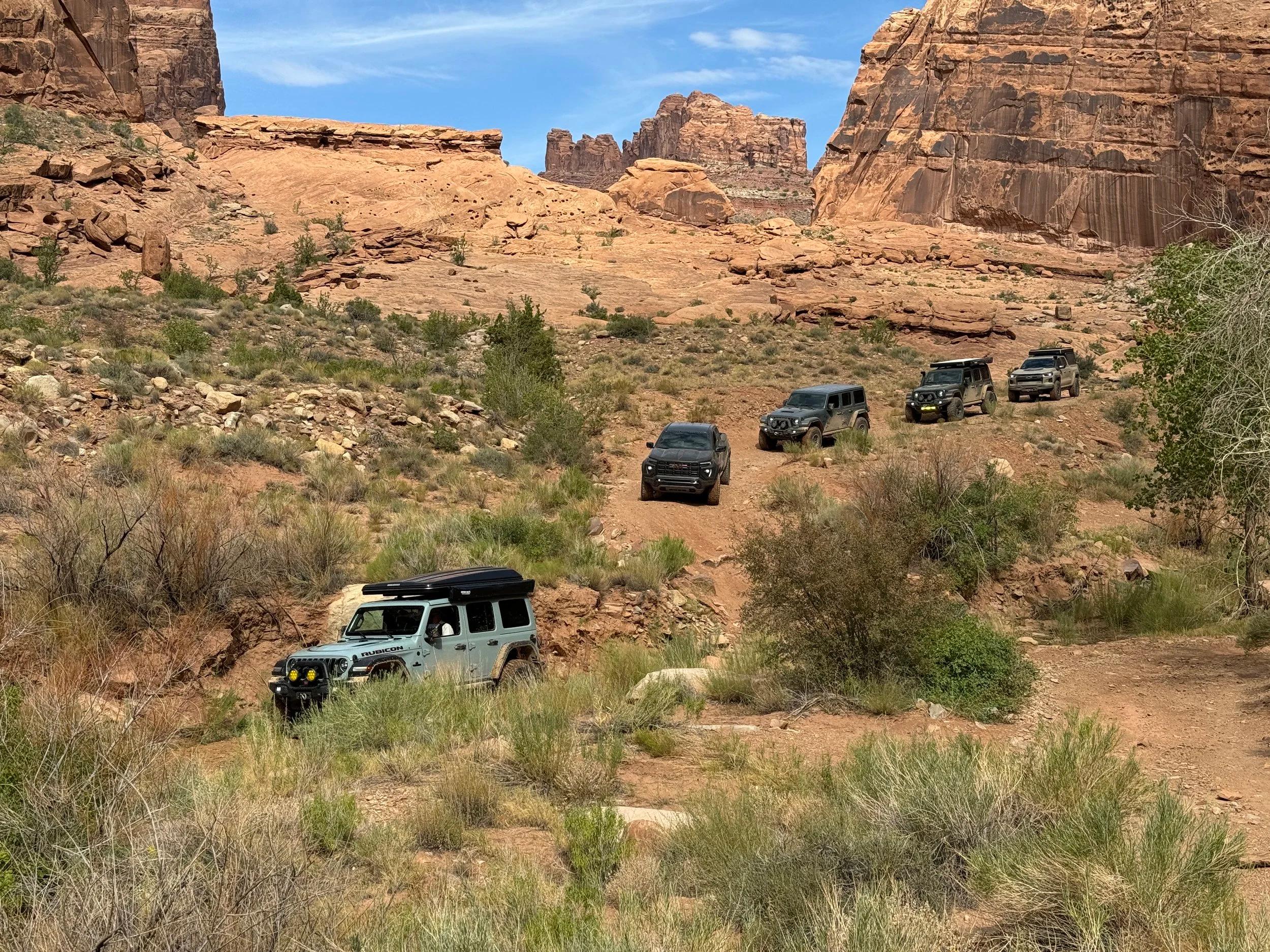 A group of off-road vehicles traveling together through a red-rock landscape