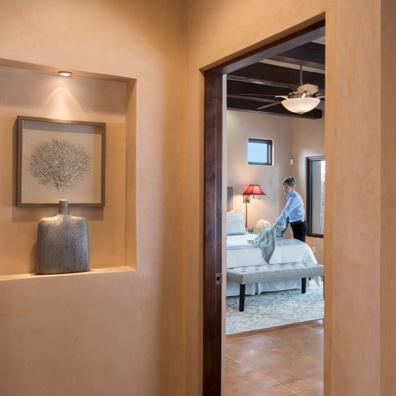 View through interior doorway of woman placing blanket on bed