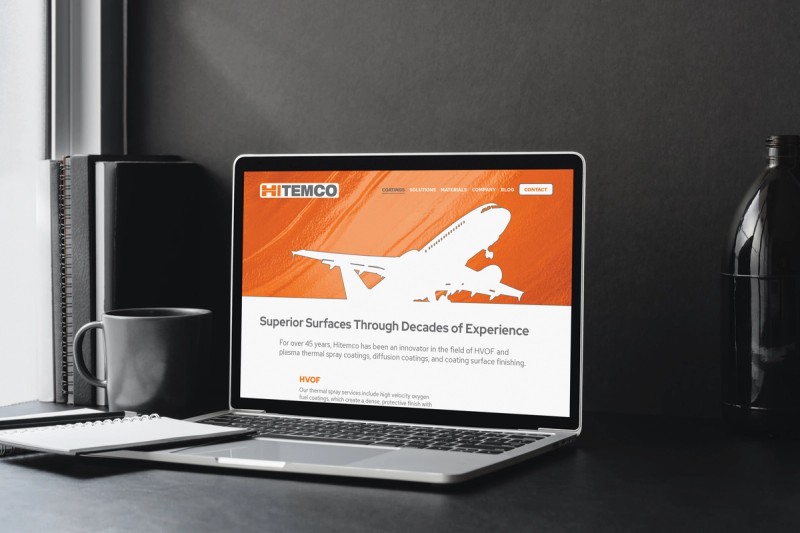 Hitemco website home page displayed on laptop in modern gray interior room with daylight