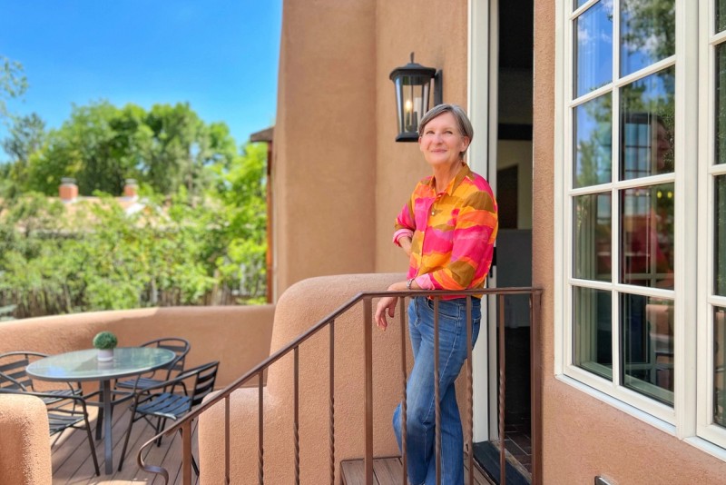 Woman in brightly colored shirt leans against railing while smiling on a sunny Santa Fe, NM patio