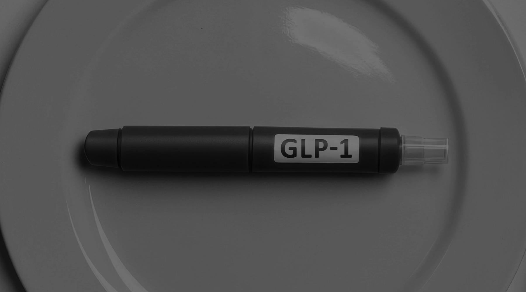 Close-up photograph of a black GLP-1 injection pen placed horizontally on a gray plate, symbolizing pharmaceutical and consumer health influences on the agribusiness and food value chain.
