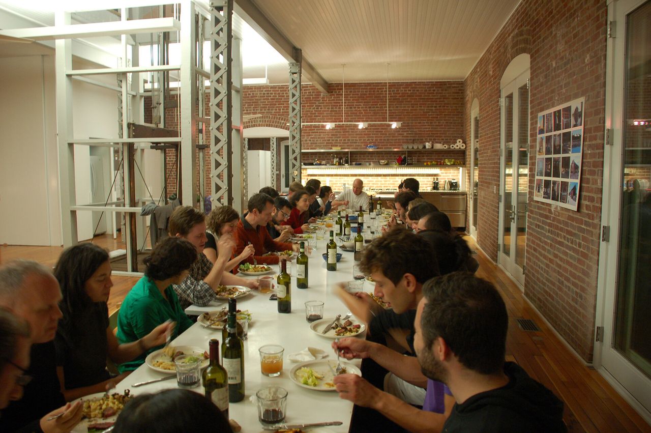 People eating on a long table in a warehouse.