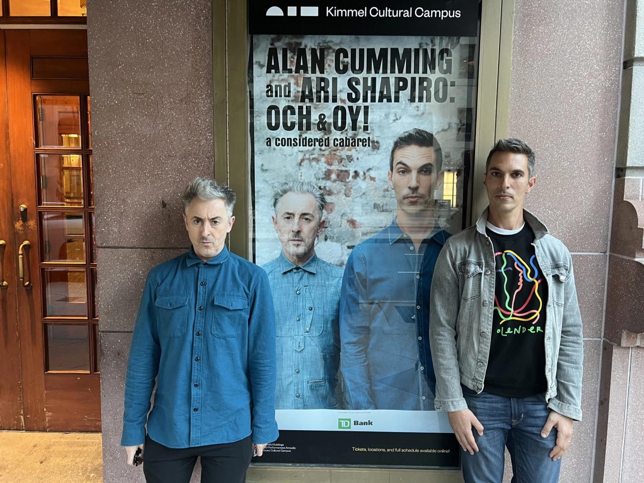 Cumming (left) and Shapiro (right) in front of a poster for Och and Oy. (Courtesy Ari Shapiro)