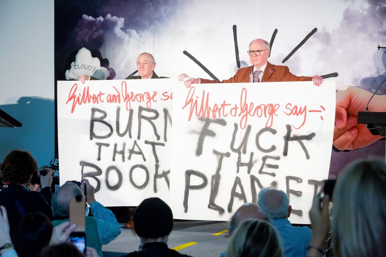 The artist duo Gilbert & George holding signs as part of “Extinction Marathon: Visions of the Future” at the Serpentine Galleries in 2014. (Photo: Benedict Johnson)