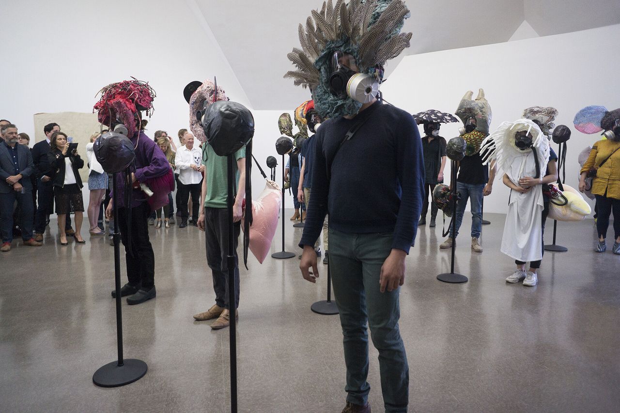 People with masks standing in an art gallery during a performance