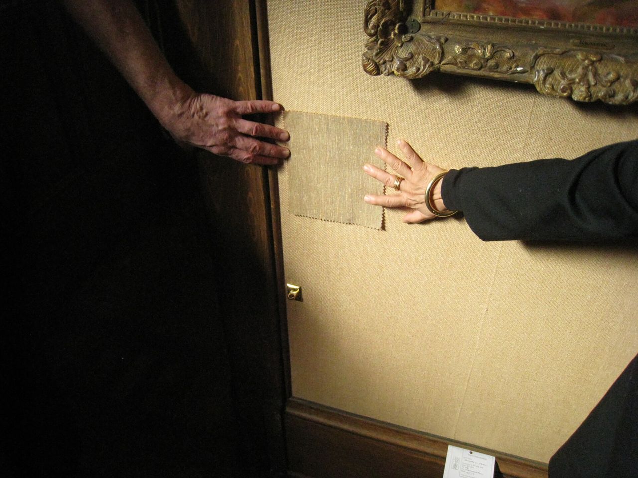 Two hands hold a piece of burlap against a burlap wall