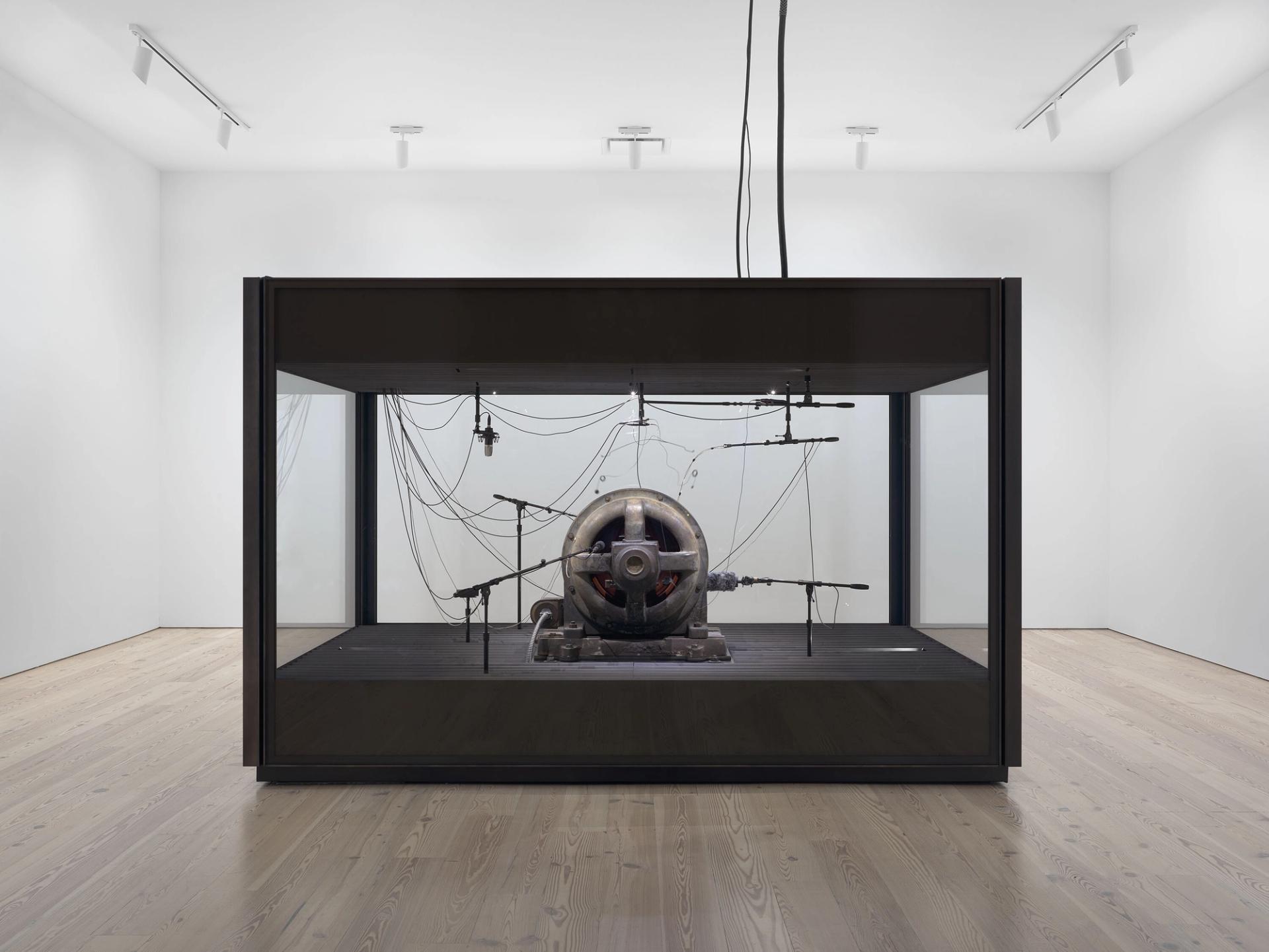 A cotton gin motor in a plexigalss box installed in an art gallery