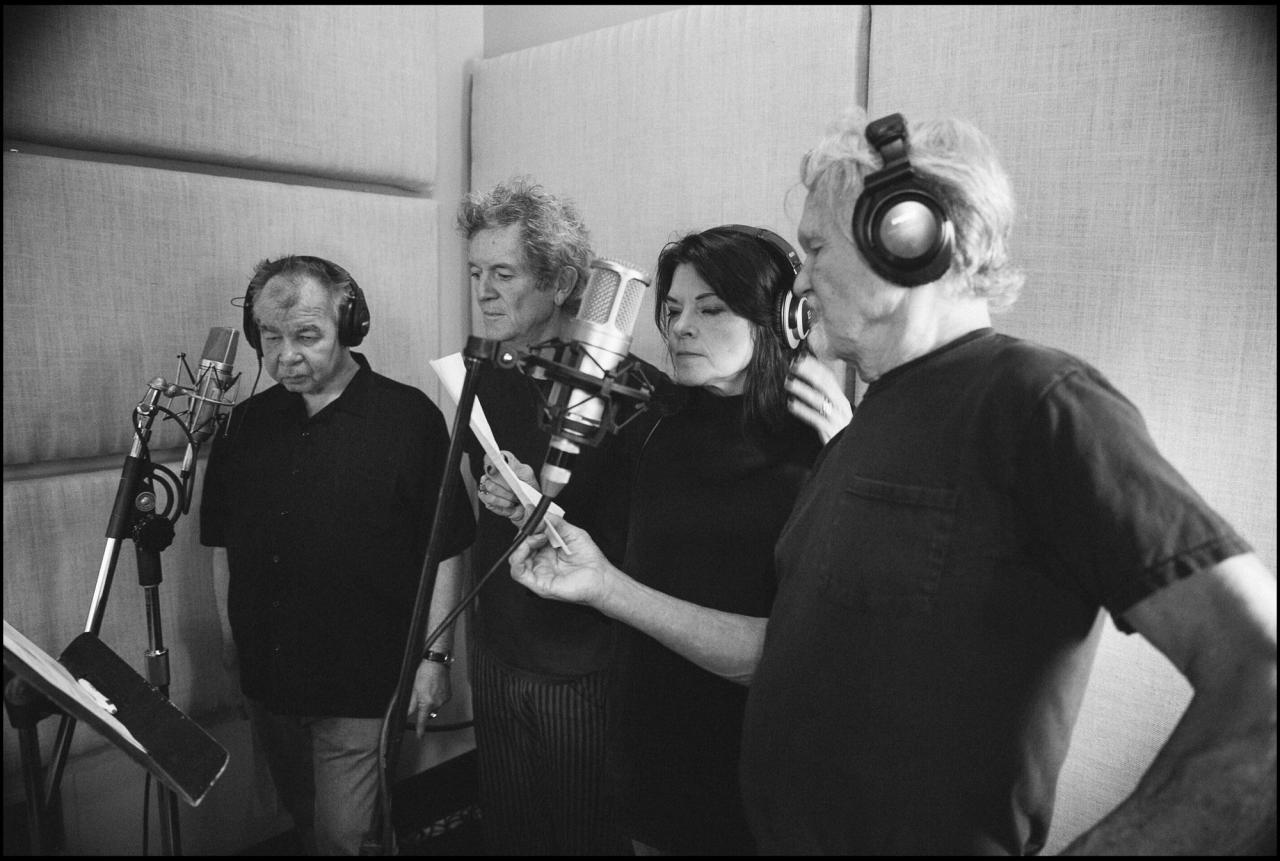 A black and white photo of four people singing in a recording studio.