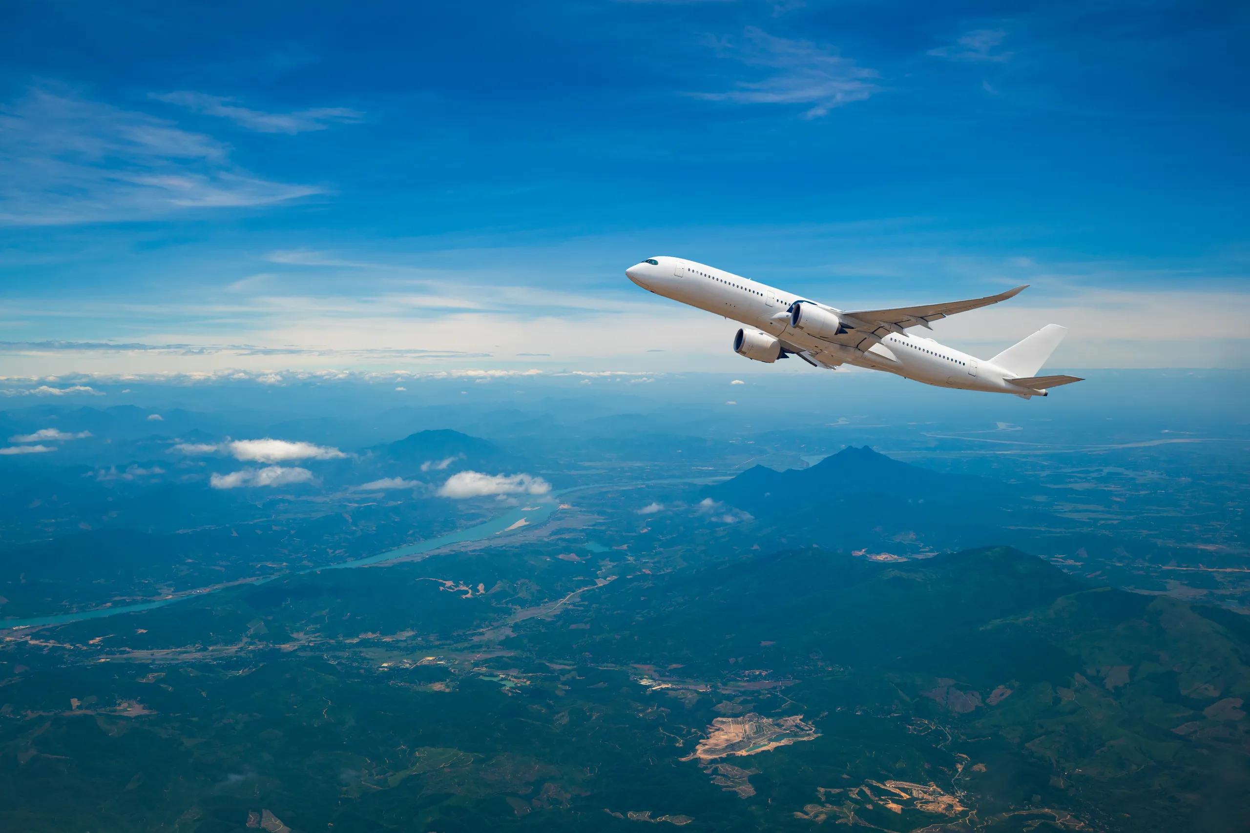 a large passenger jet is flying over a mountain range .