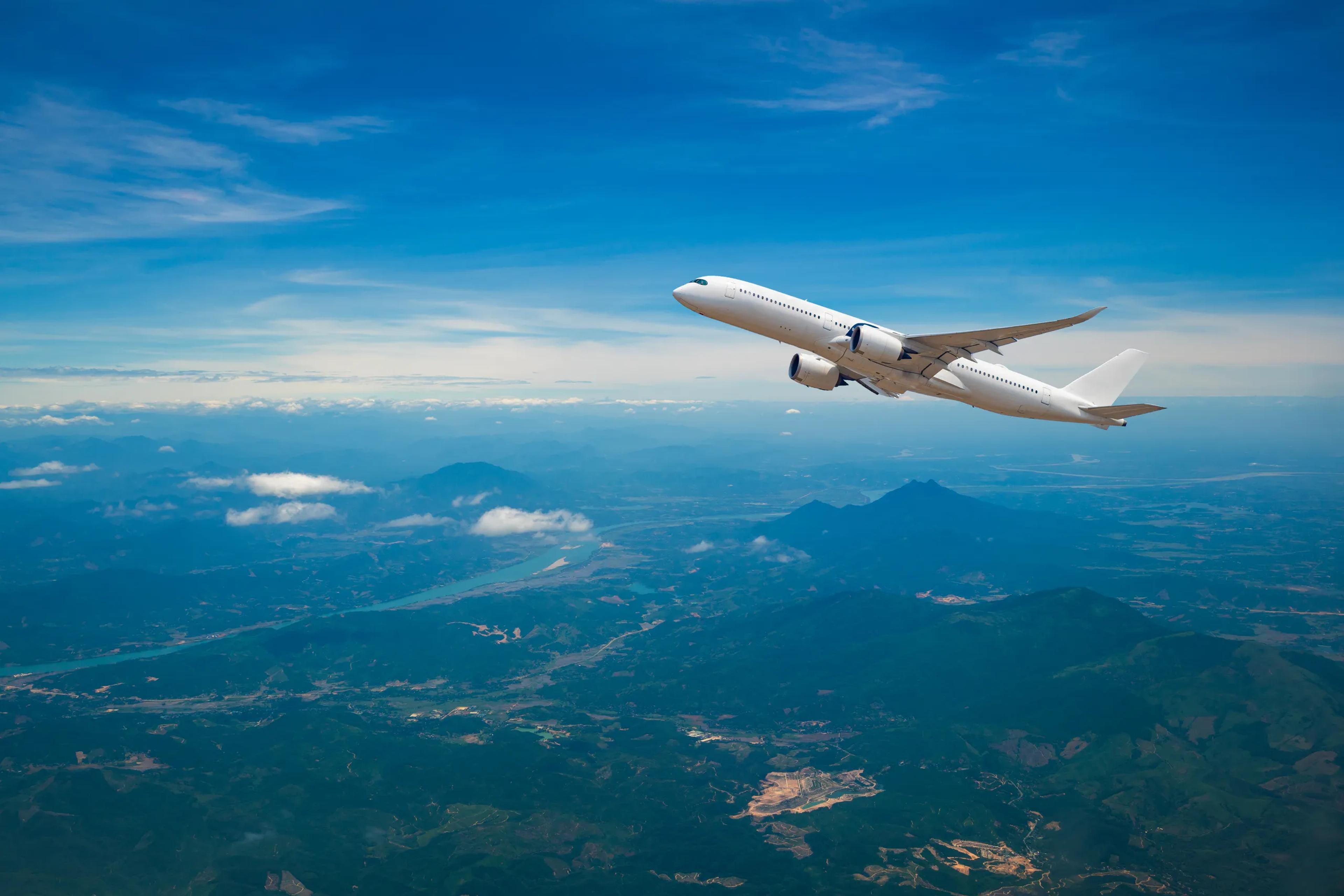 a large passenger jet is flying over a mountain range .
