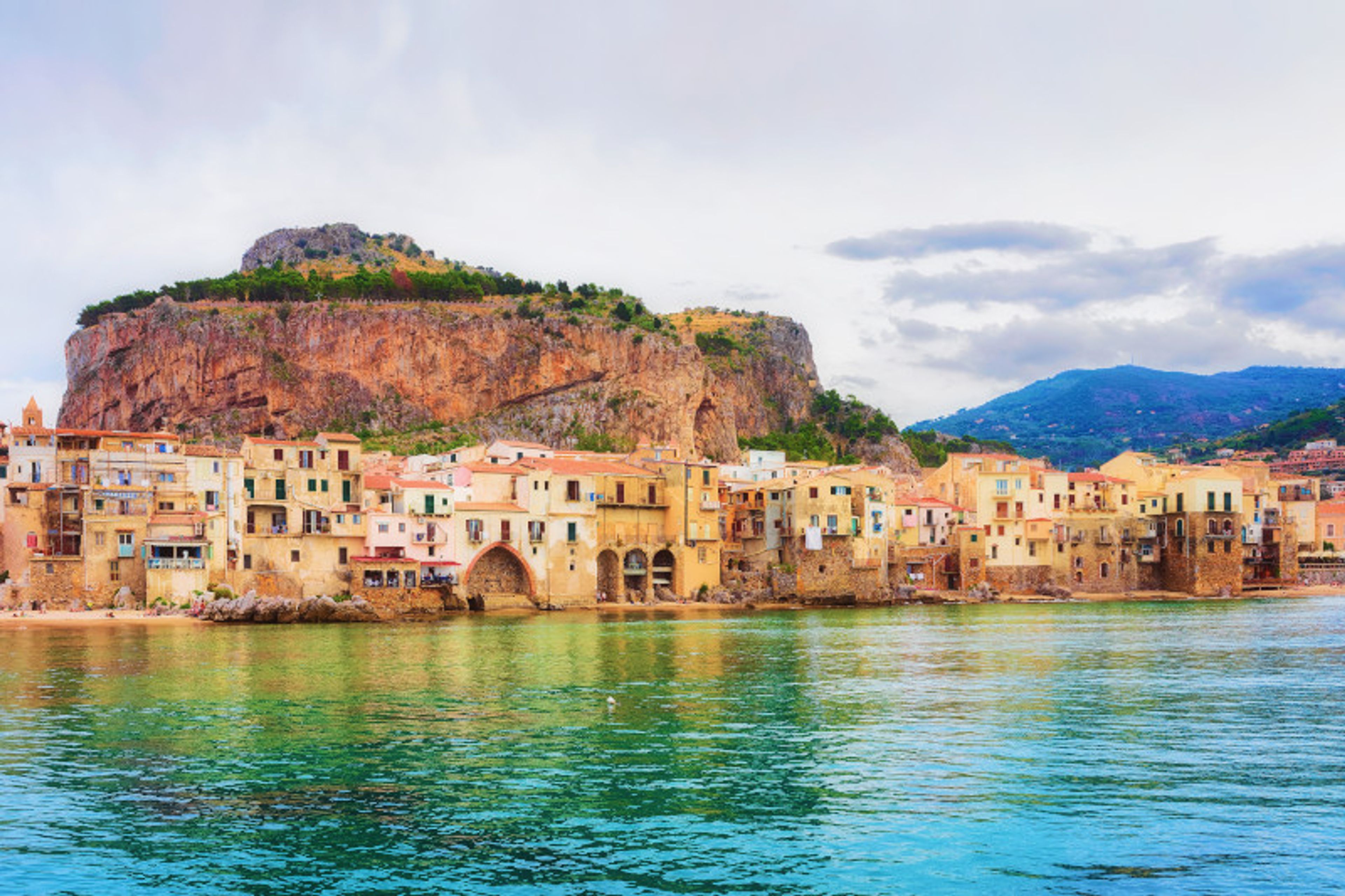 a small town in the middle of a body of water with mountains in the background .