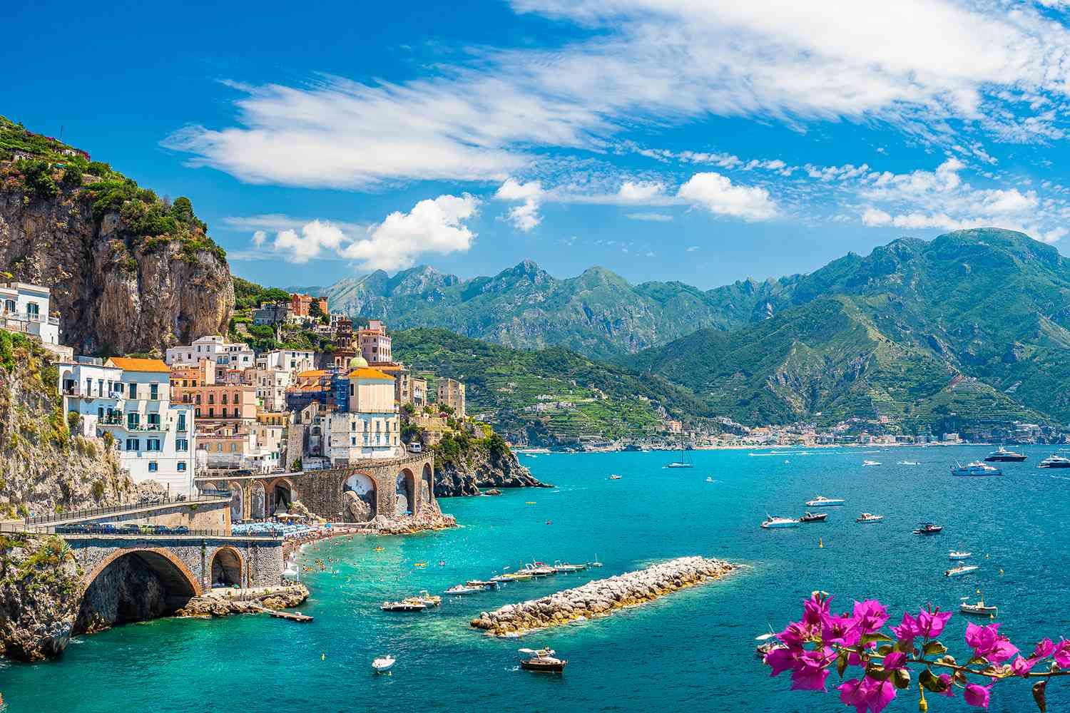 a small town on the coast of italy with boats in the water and mountains in the background .